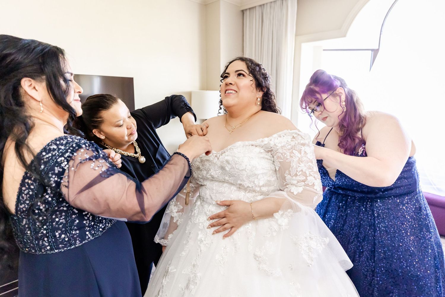 Bride getting ready with help from bridesmaids in blue dresses.