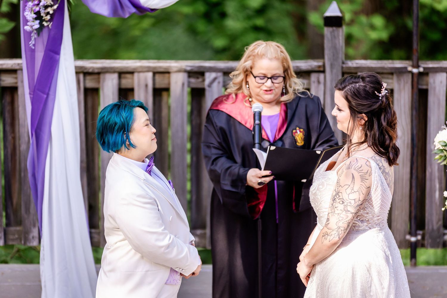 An intimate wedding ceremony moment under a purple-draped arch in a woodland setting.