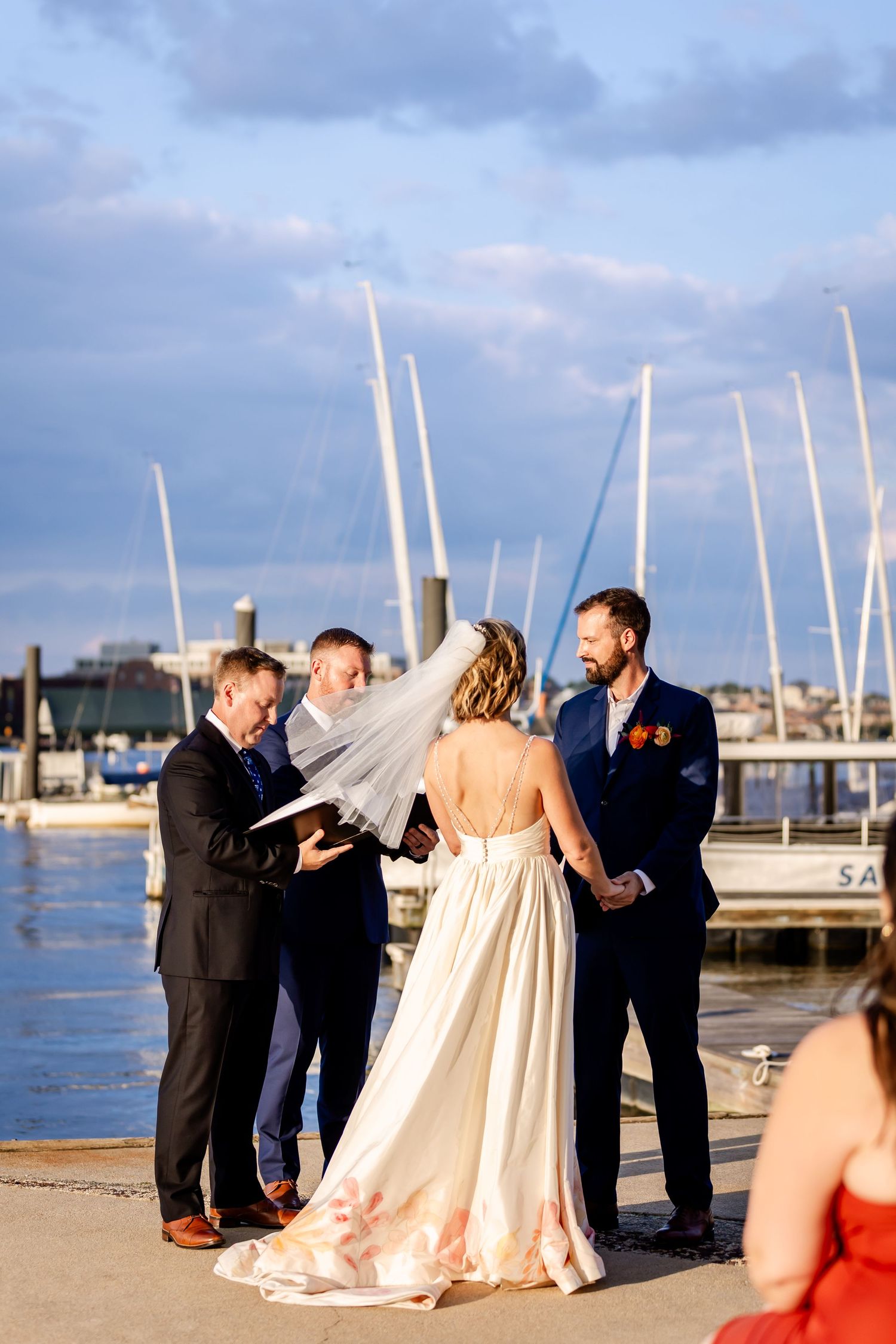 Wedding ceremony takes place on dock with sailboats and marina setting in background.