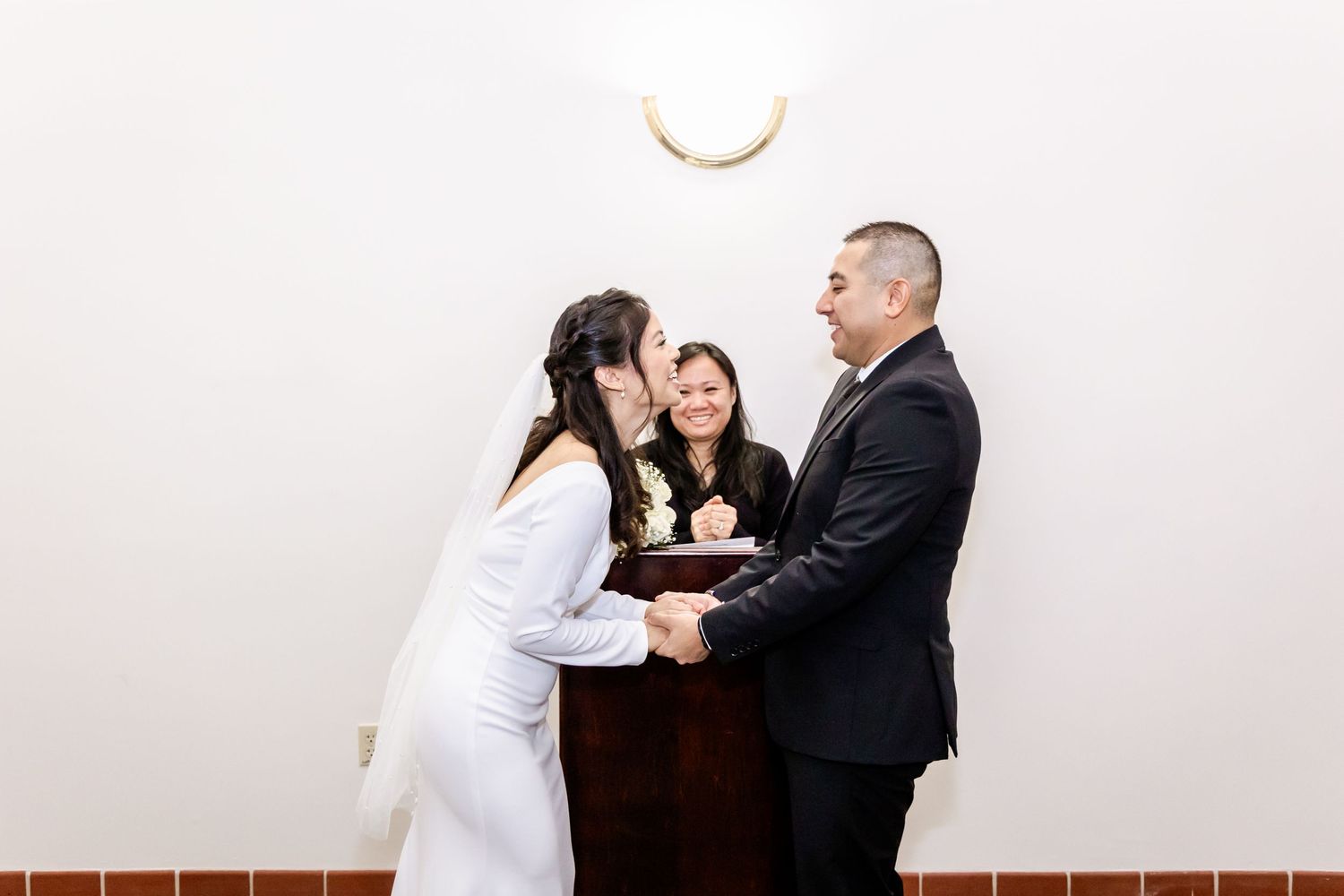 A couple exchanges vows during an intimate indoor wedding ceremony with an officiant present.