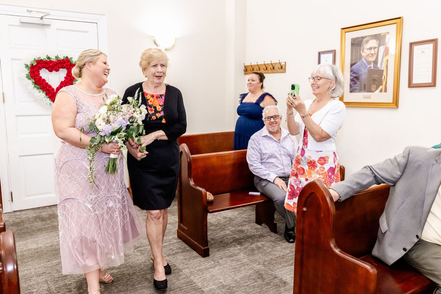 People gather in a chapel with red heart decor and floral arrangements.