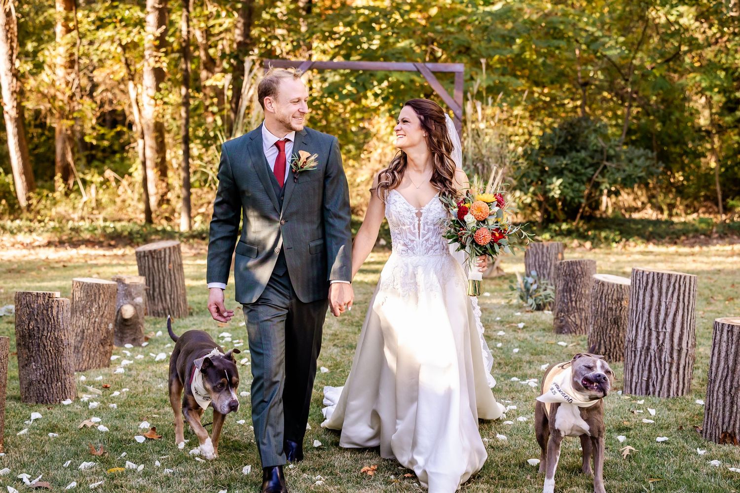 A couple walks their dog during their wedding photoshoot in a wooded area.