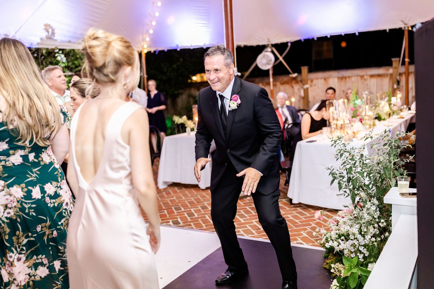 Energetic dancing scene at a wedding reception under a tent with elegant table settings in the background.