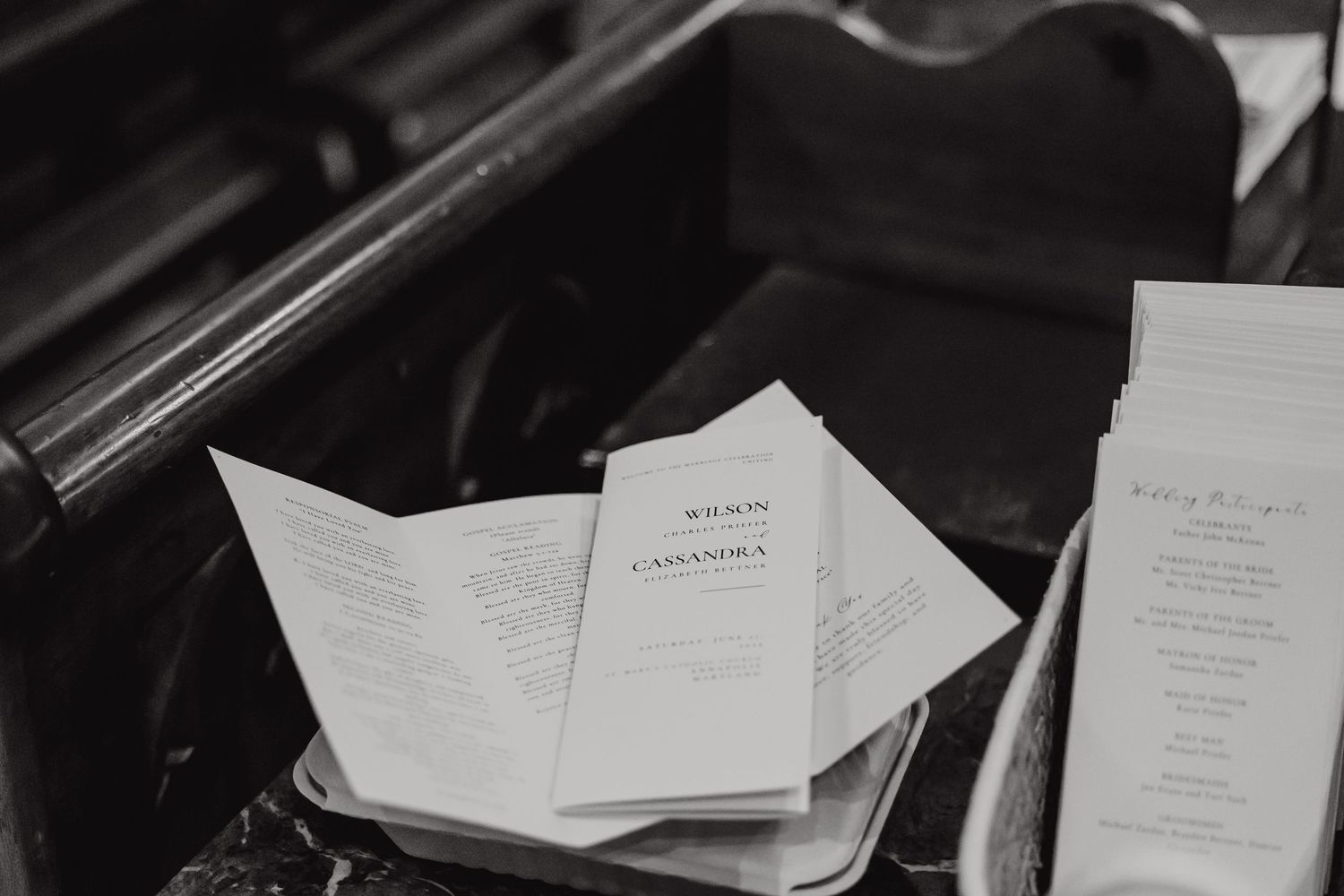 Black and white photo of wedding ceremony programs displayed in church pew.