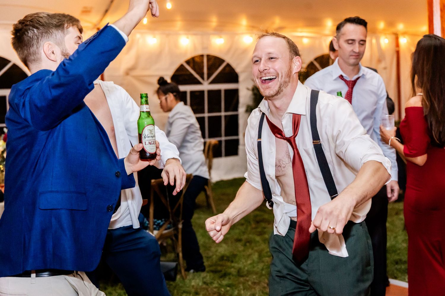 Energetic wedding guests dance and celebrate on the dance floor under a reception tent.