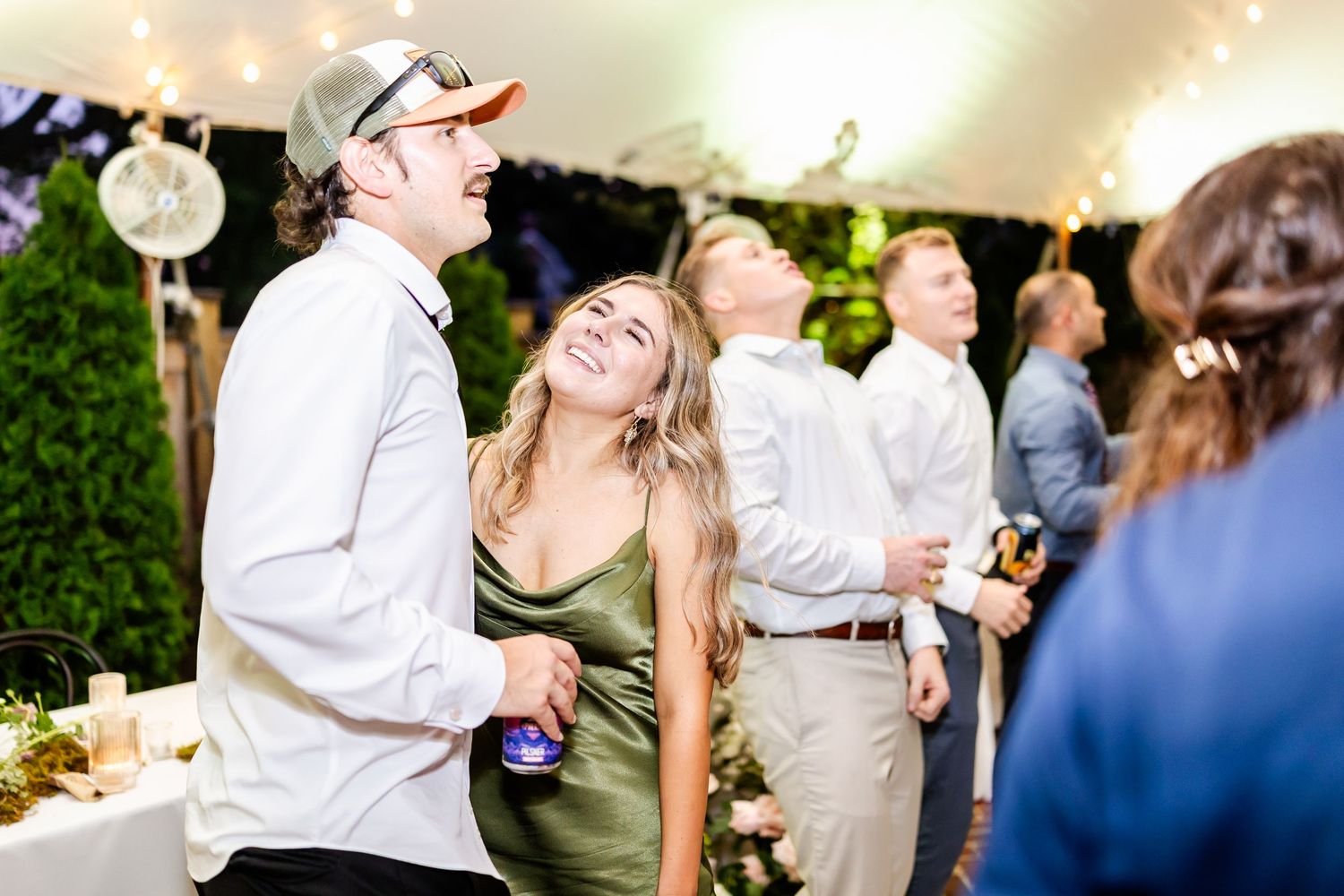 Guests dancing and celebrating at an outdoor evening wedding reception under twinkling lights.