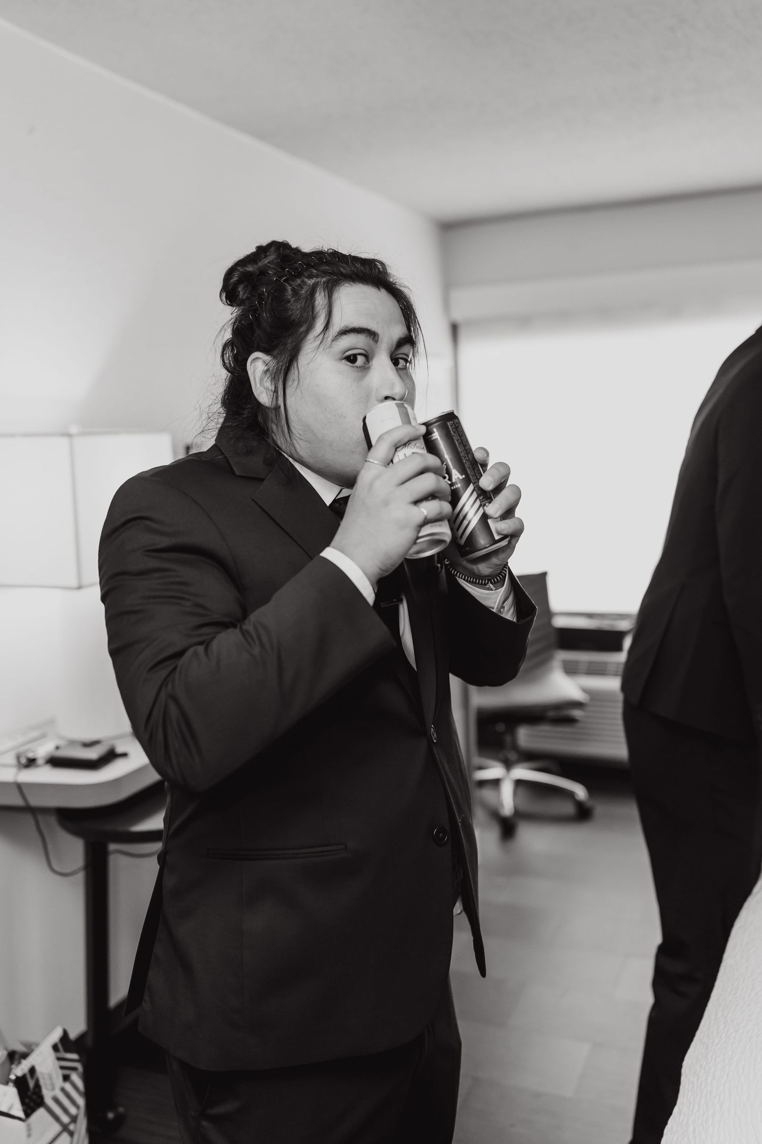 A person in a black suit holds a phone to their ear while standing in a white office space.