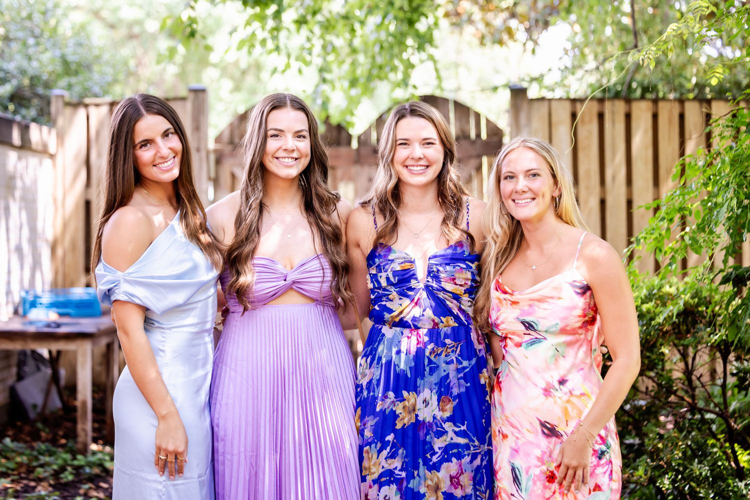 Bridesmaids wearing purple and floral dresses pose together in an outdoor garden setting.