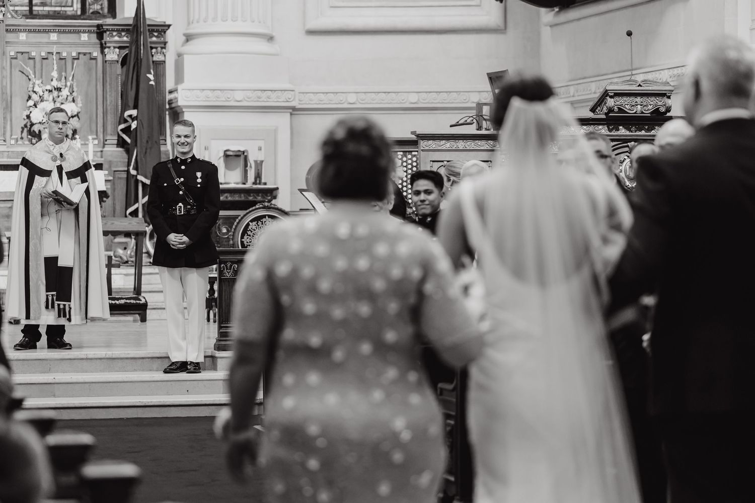 Black and white photo of wedding guests observing ceremony in formal venue.