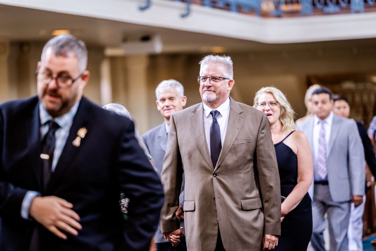 Wedding guests in formal attire watching ceremony proceedings in elegant venue.