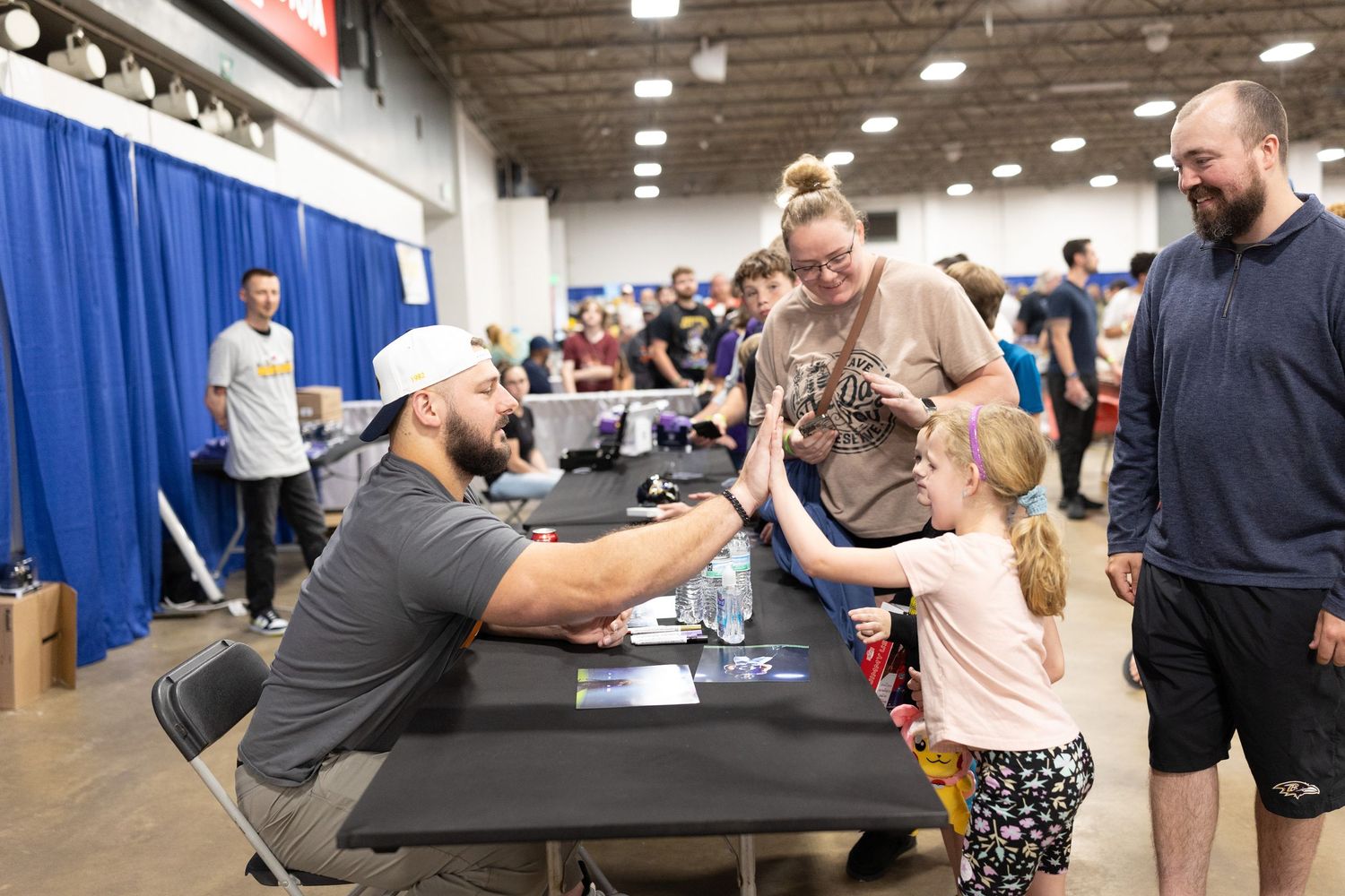 Row of people seated at tables during a convention or signing event.