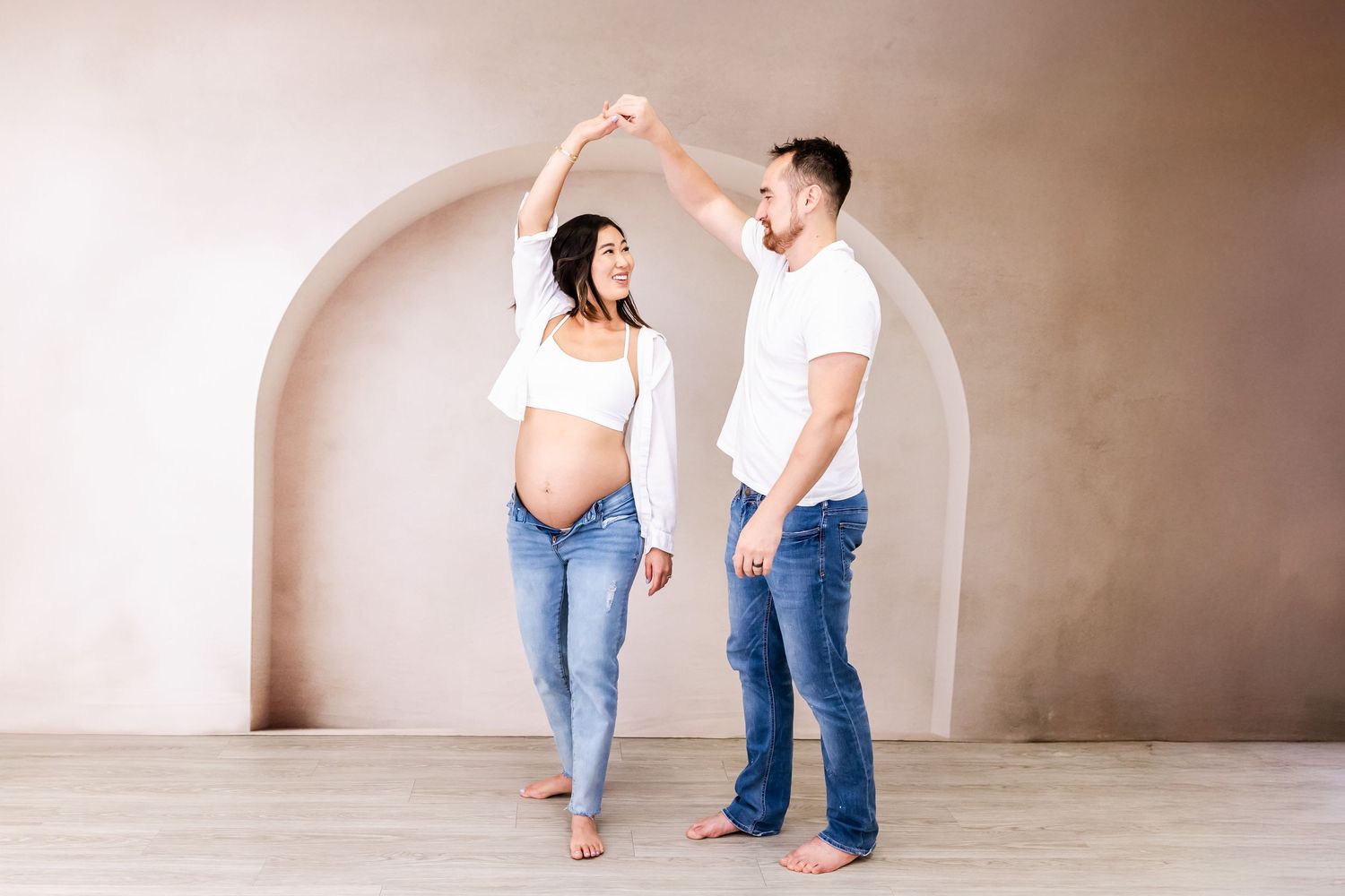 A couple in jeans and white shirts dance together in a series of romantic poses against a neutral studio backdrop.