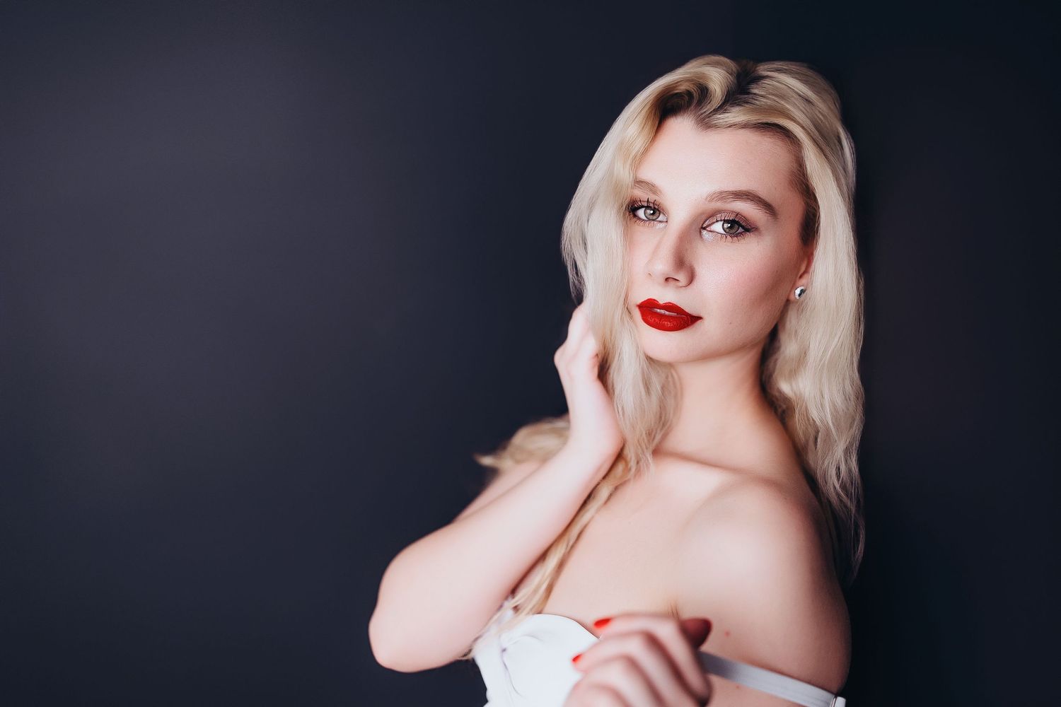 Portrait of a blonde woman in white top wearing bright red lipstick against a dark background.