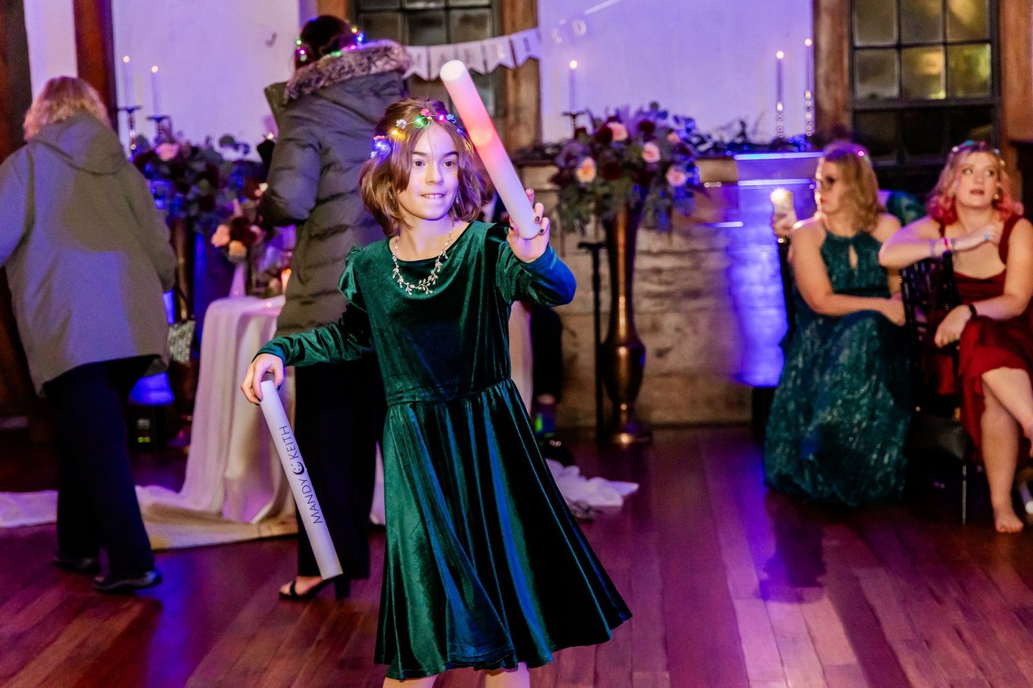 Wedding guest in emerald green dress dancing under purple lighting.