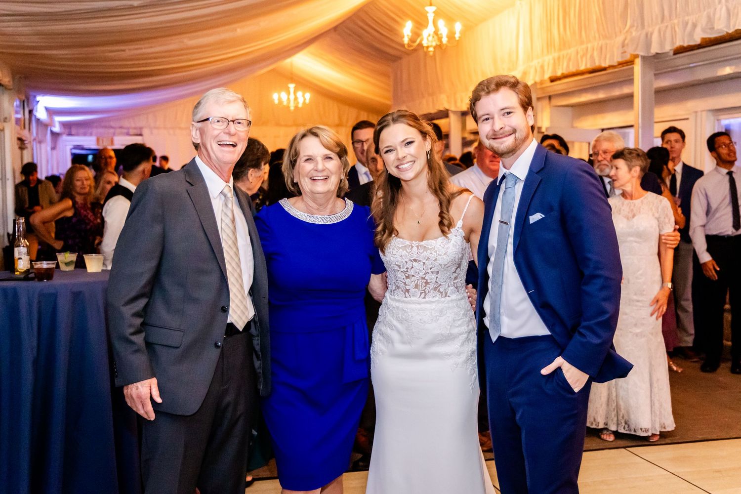 Wedding celebration in an elegant white draped venue with chandelier and formal attire.