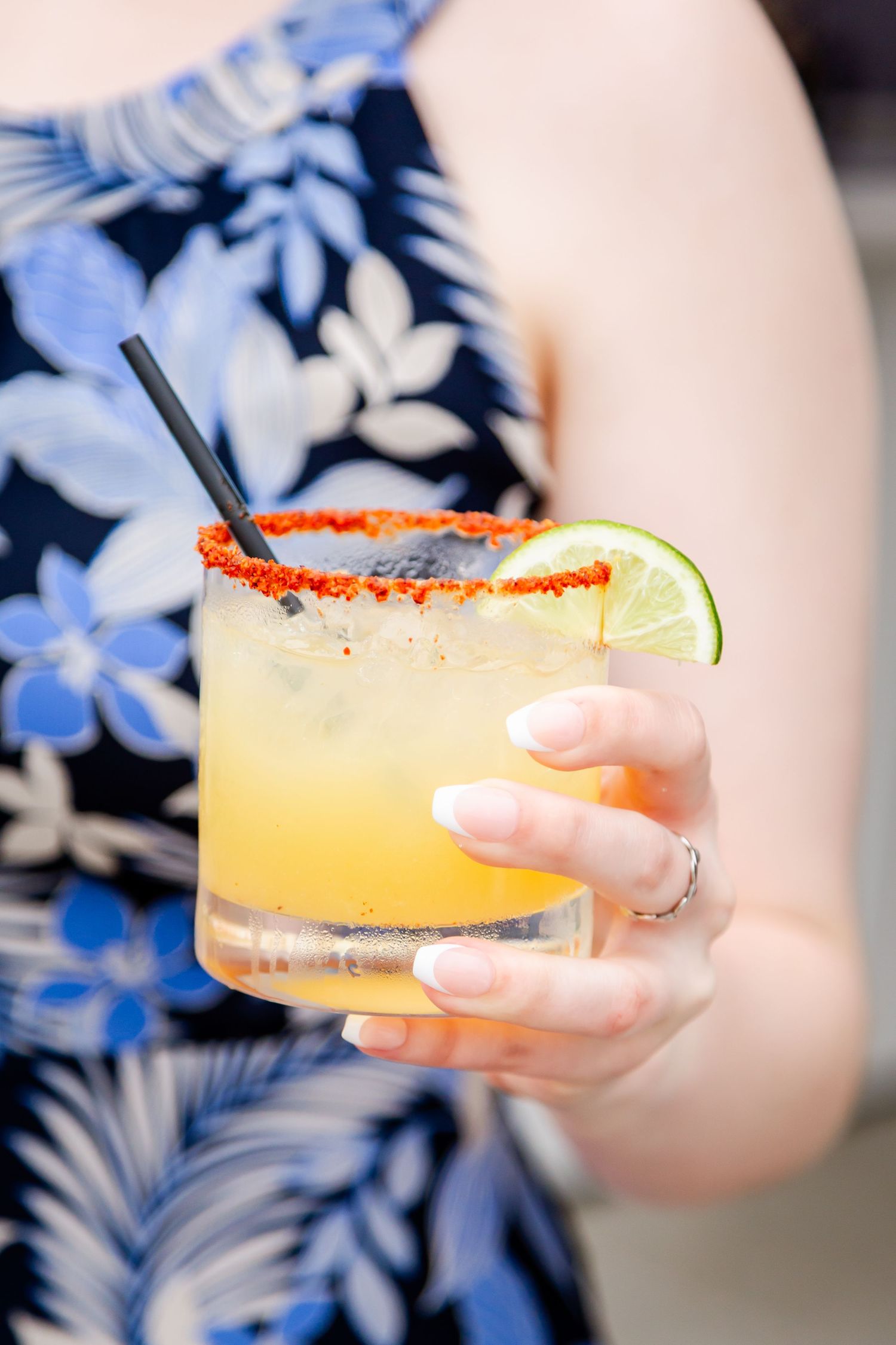 A margarita cocktail with lime and chili salt rim held against a blue floral print dress.