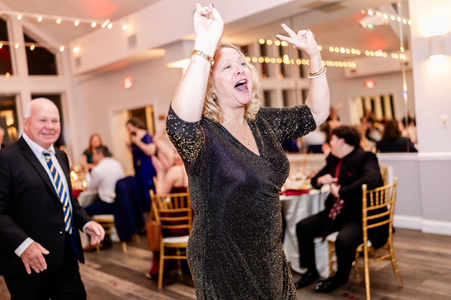 Wedding reception guests dancing and celebrating in an indoor venue with string lights.