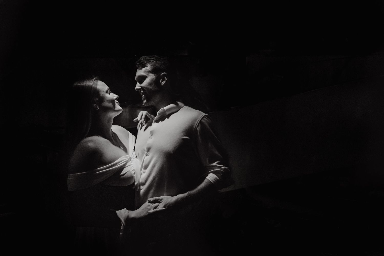 A romantic couple dances intimately together in dramatic black and white lighting.