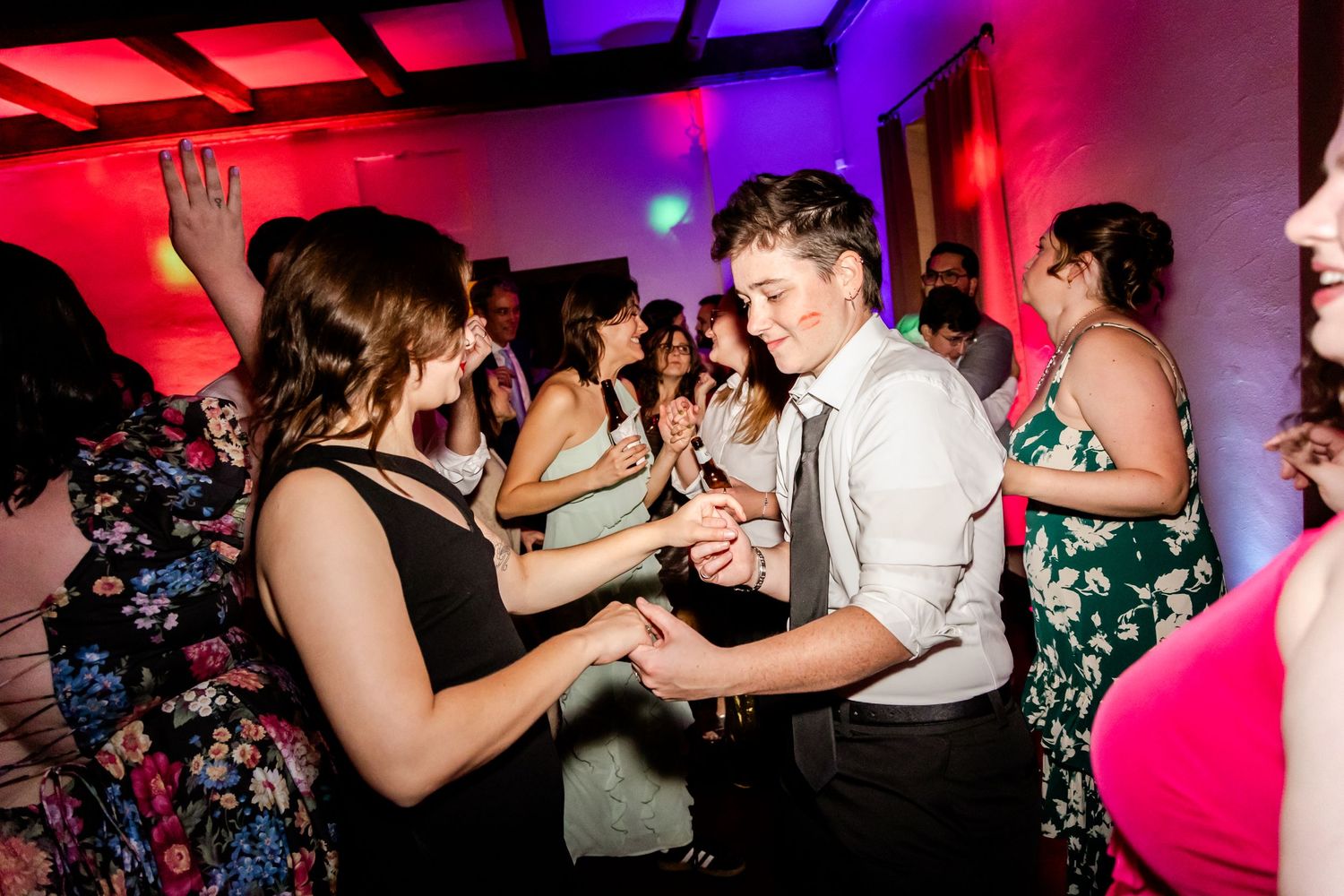 Couples dancing at a wedding reception with dramatic red and purple lighting.