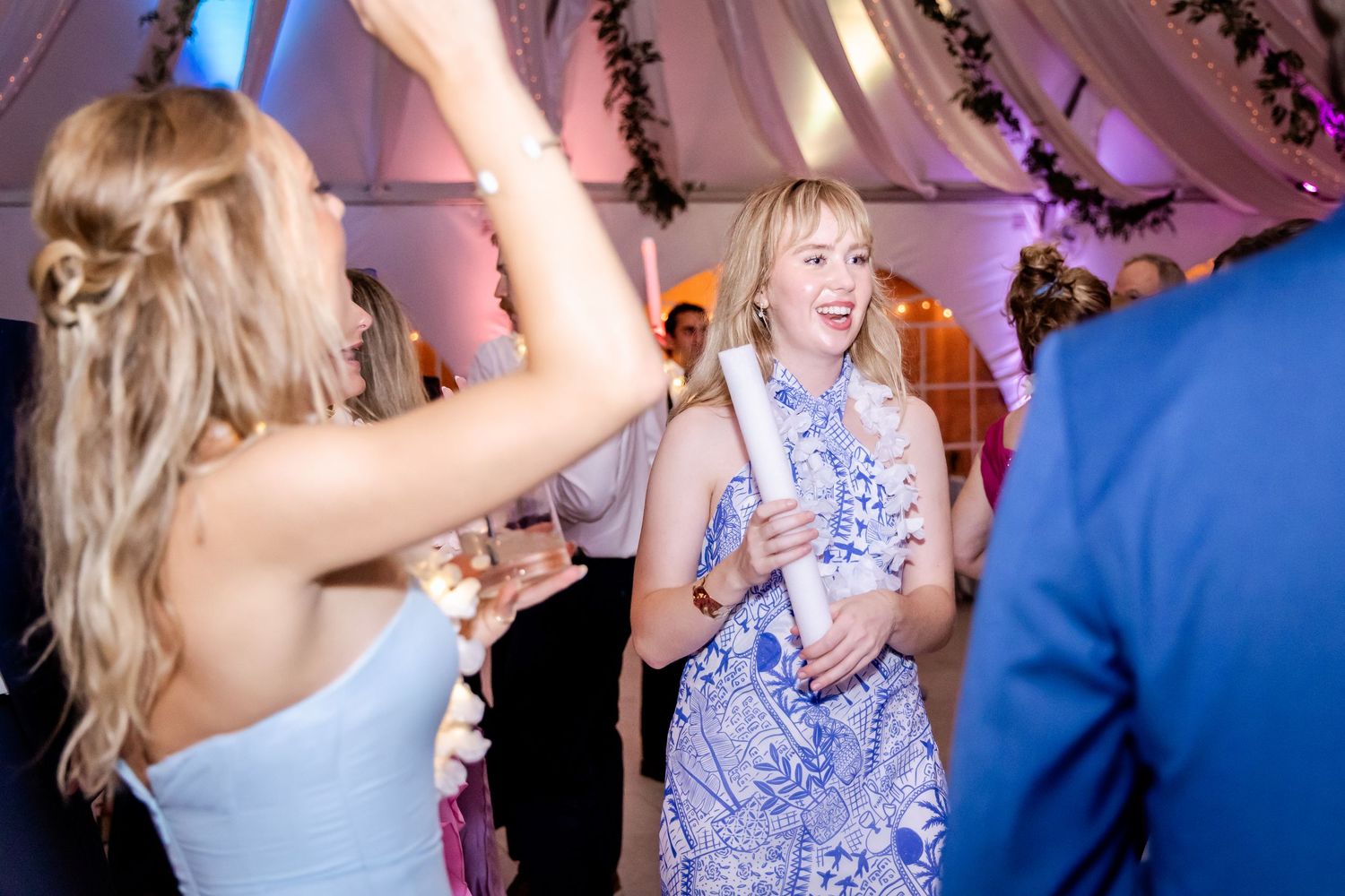 Wedding party dancing and celebrating under purple-lit tent decorations.