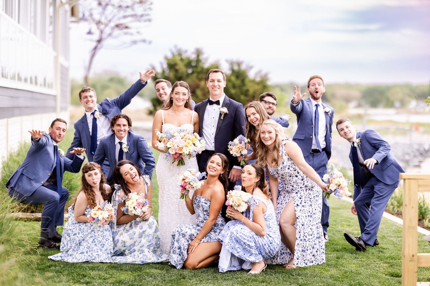 Wedding party lounging and laughing together on a grassy hillside.