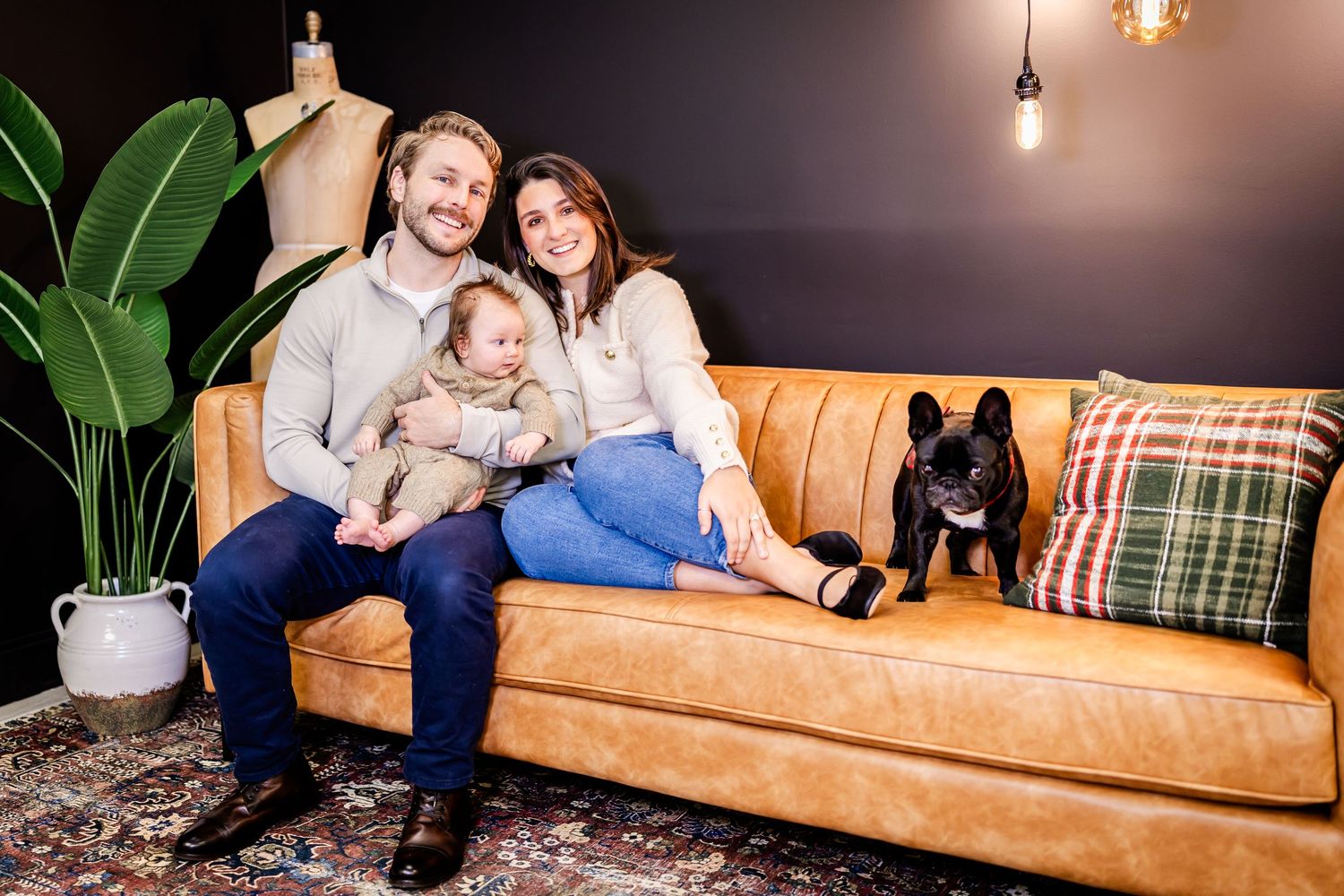 A relaxed family moment on a tan leather couch with their French Bulldog and a large houseplant in the background.