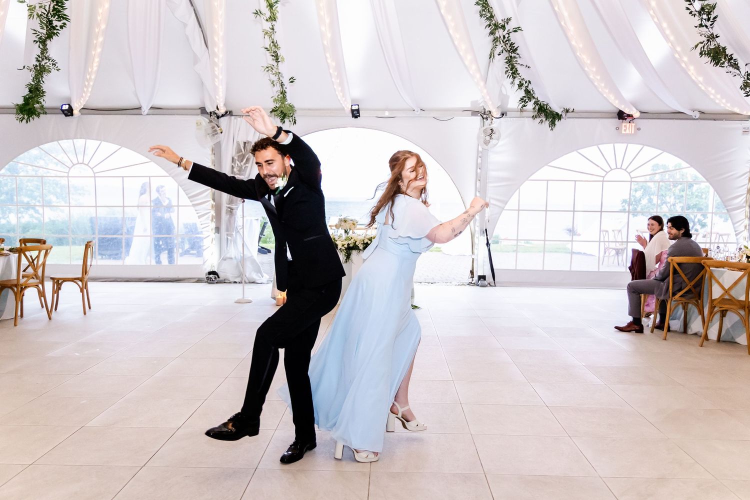 Wedding couple dances in an elegant white tent decorated with greenery garlands.