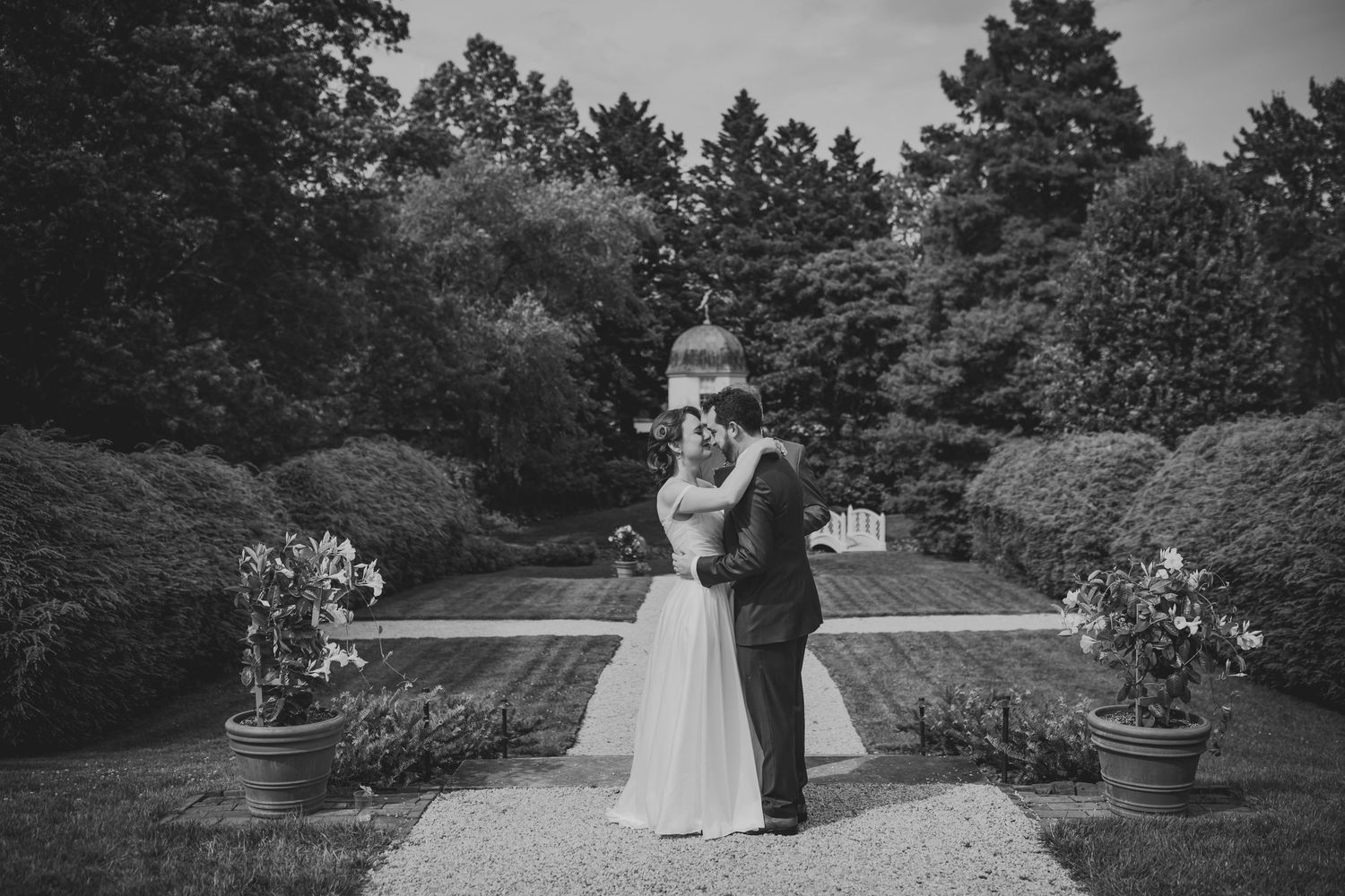A couple shares a romantic moment in a garden setting during a black and white wedding photoshoot.