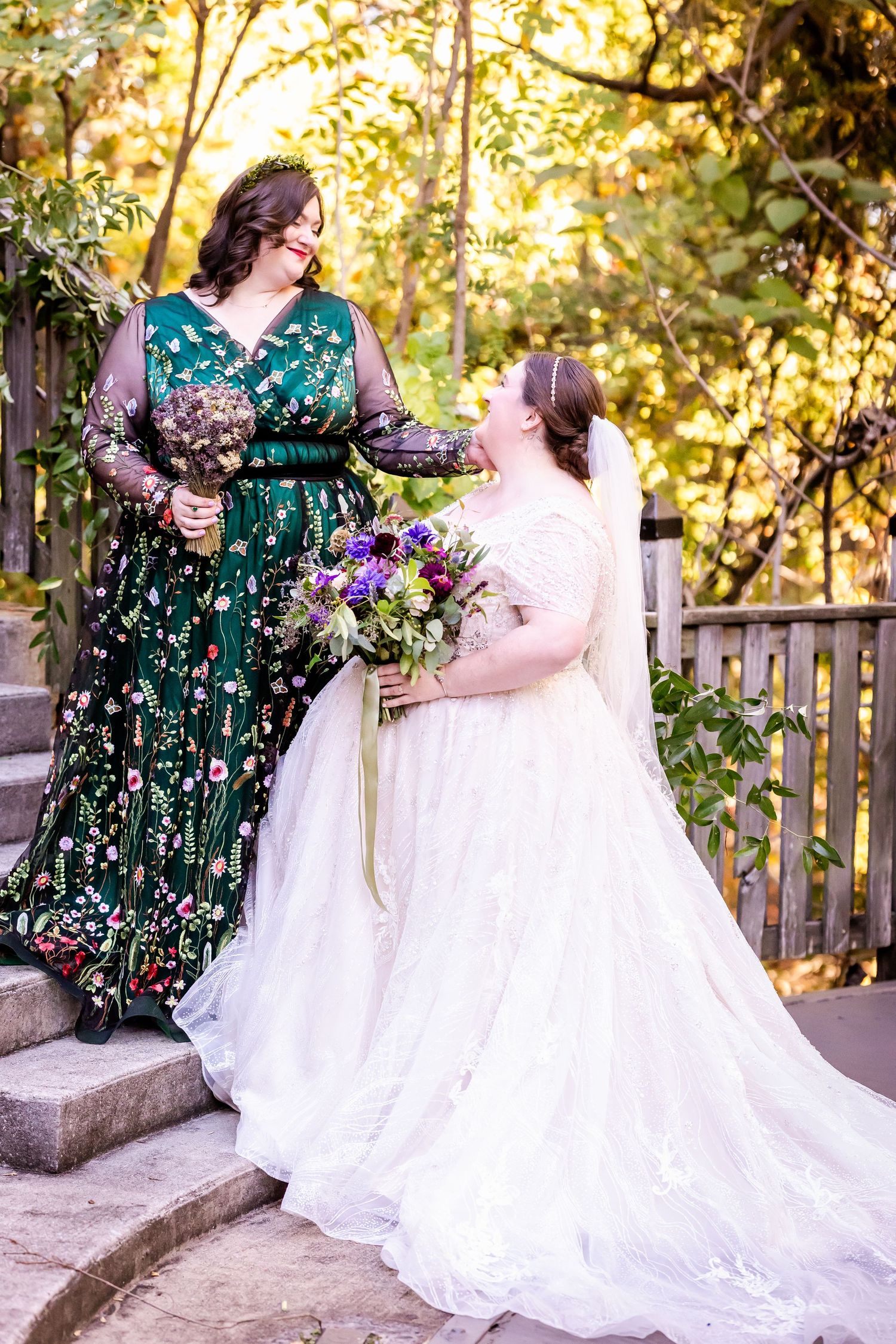 Two people in wedding attire share a joyful moment with purple flower bouquets on stone steps.