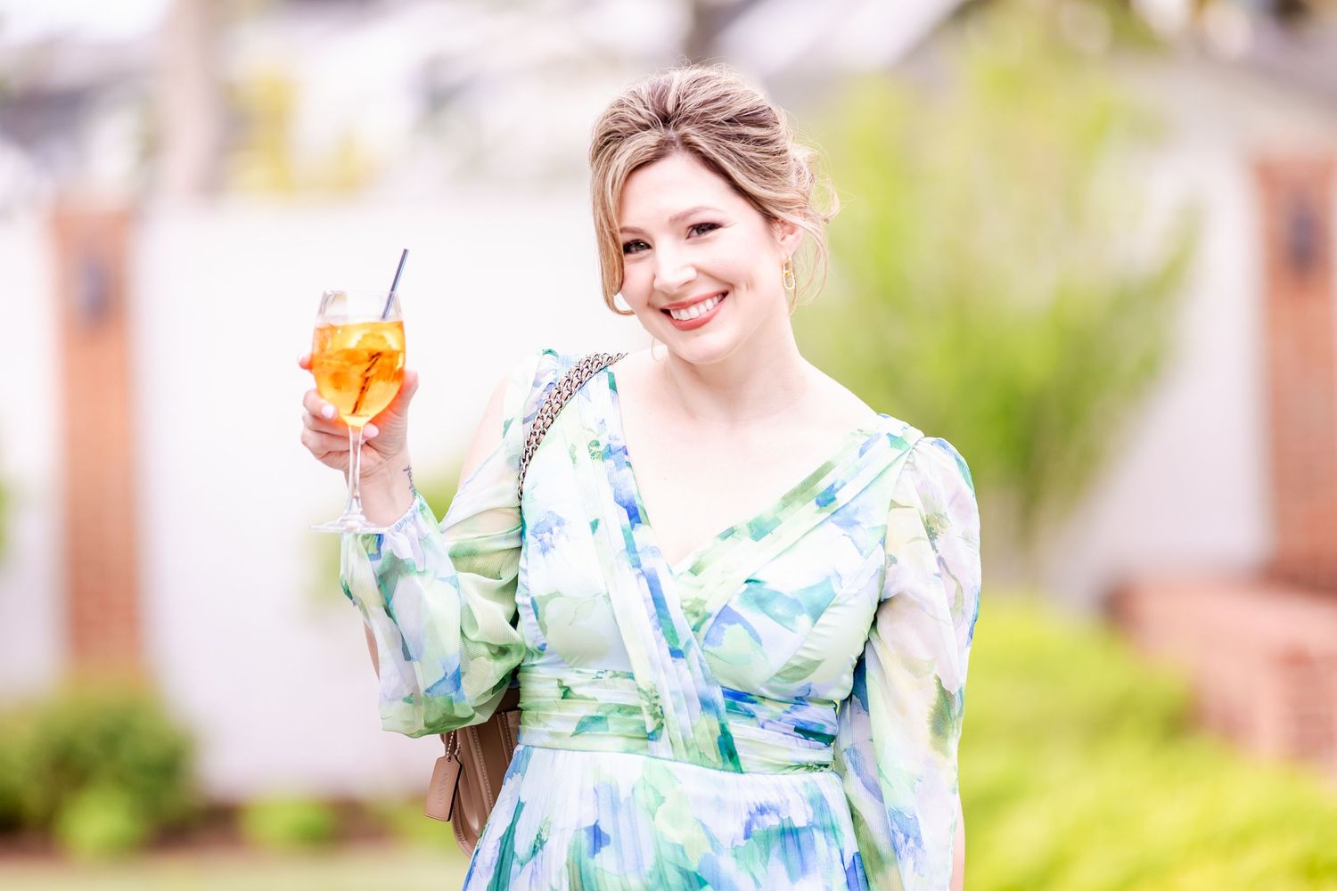 Woman in floral print dress holding a cocktail at outdoor event.