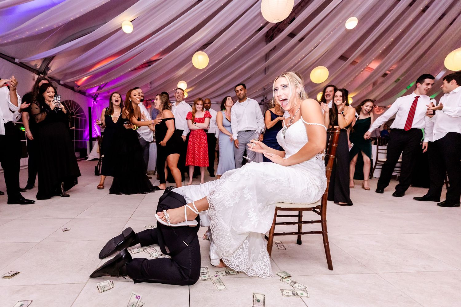 A wedding reception under a draped tent ceiling with purple lighting as guests gather around for a traditional activity.