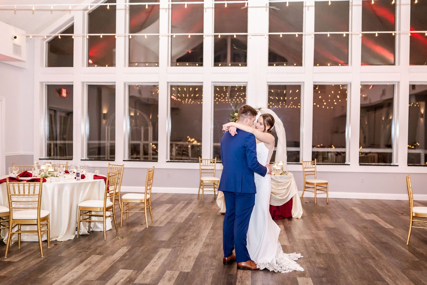 Wide view of wedding reception venue with hardwood floors and string lights.