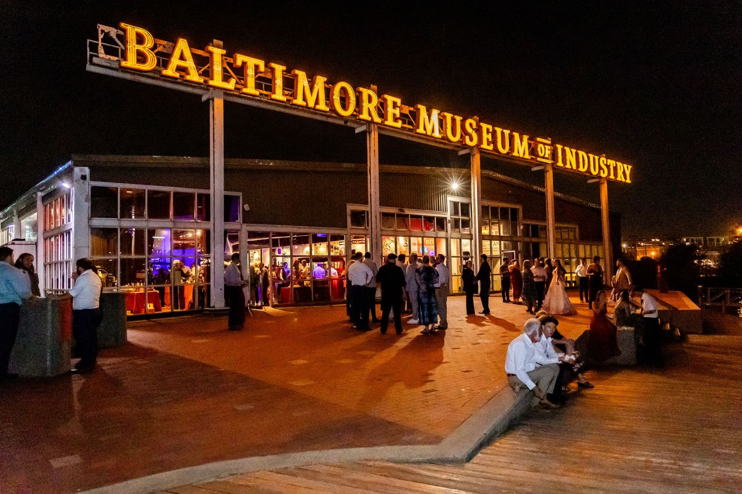 Illuminated Baltimore Museum sign at night with visitors gathered outside on the waterfront.
