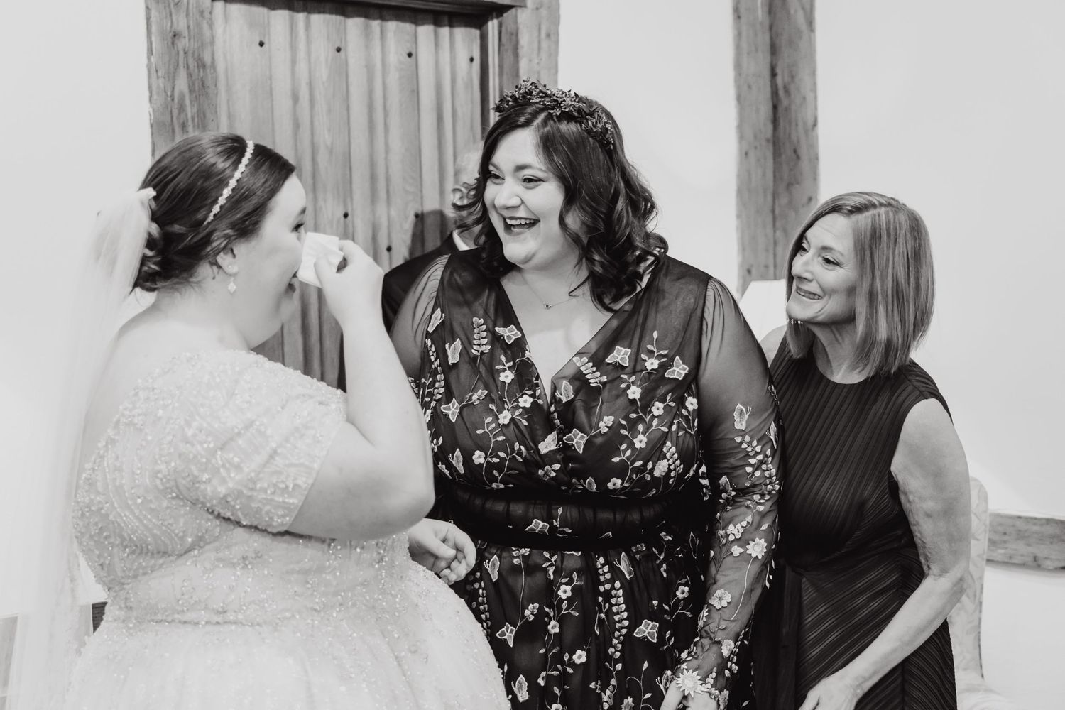 Three women share a candid laughing moment at a wedding celebration.
