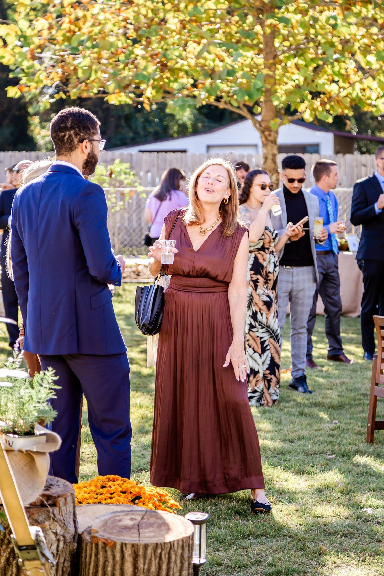 Guests mingle at an outdoor reception with autumn trees in the background.