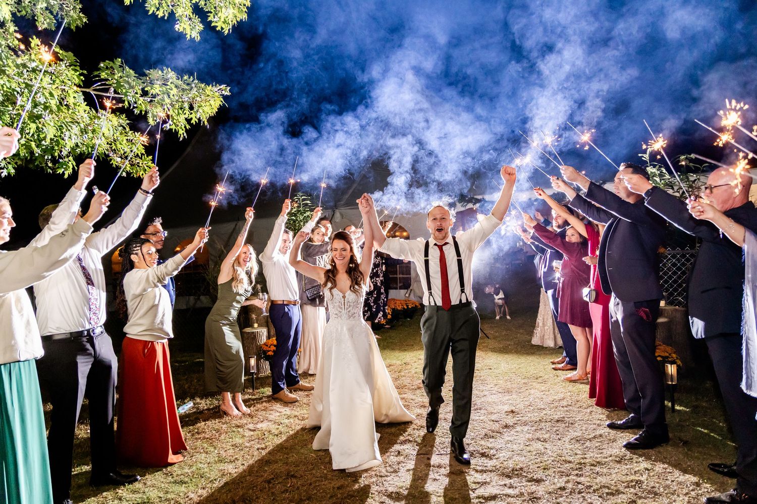 Wedding celebration with sparklers creating trails of light against a dark blue evening sky.