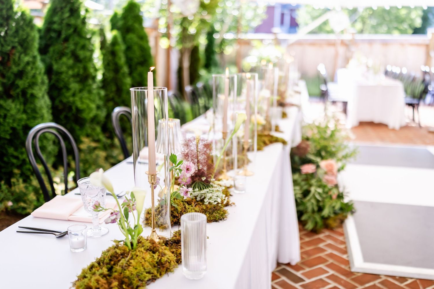 Outdoor wedding reception setup with white linens and greenery on elegant tables.