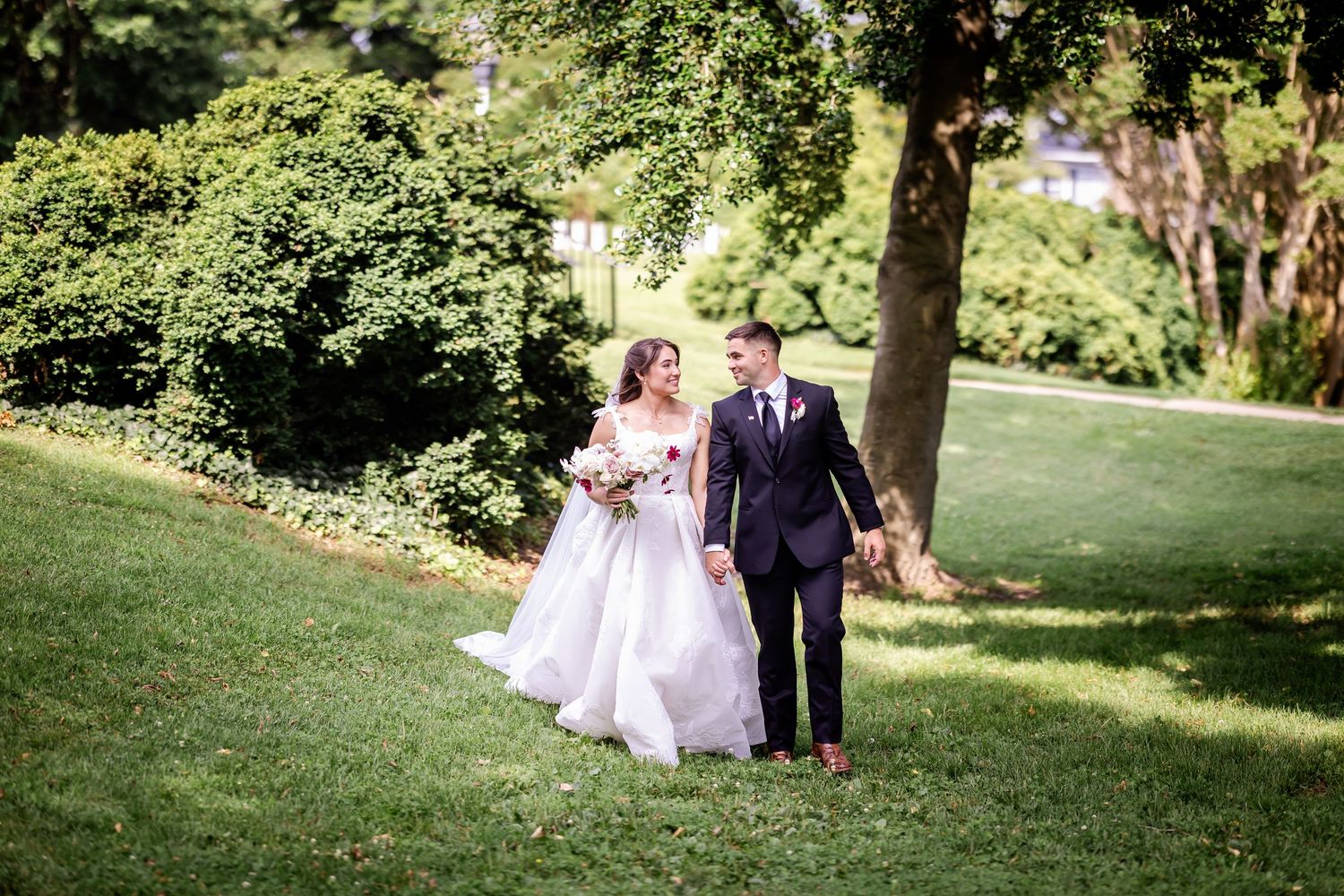 Wedding party walking through lush green garden setting on sunny day.