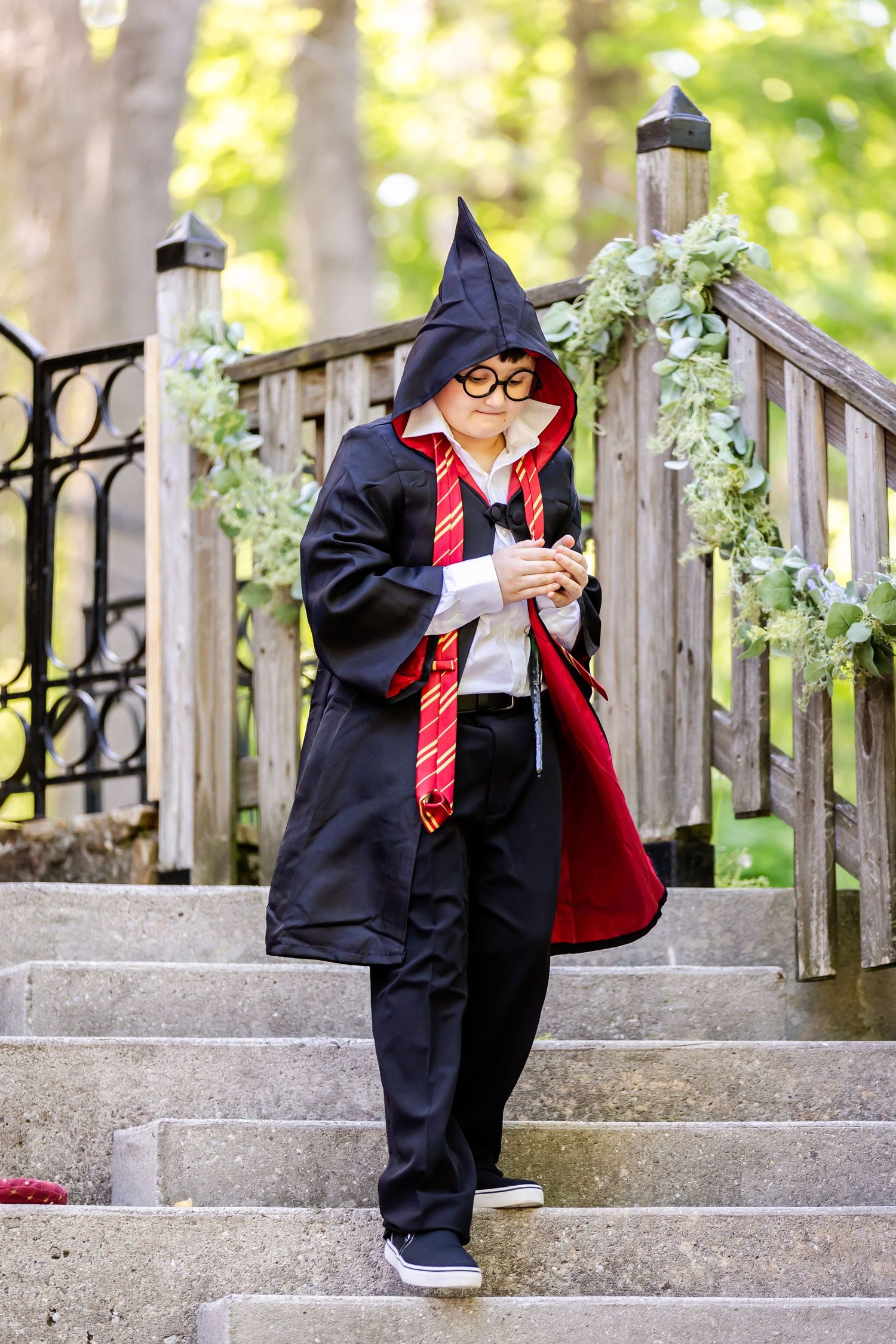 Person in Harry Potter costume with wizard robe and red tie poses on stone steps with floral decor.