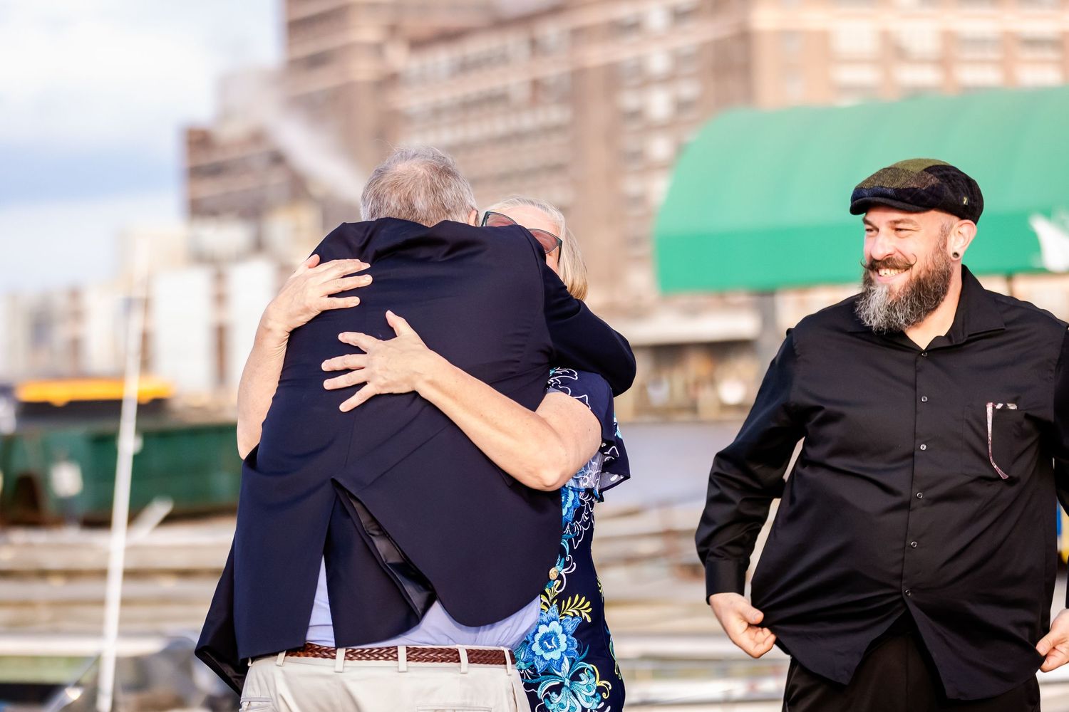 Emotional embrace between guests at outdoor waterfront celebration.