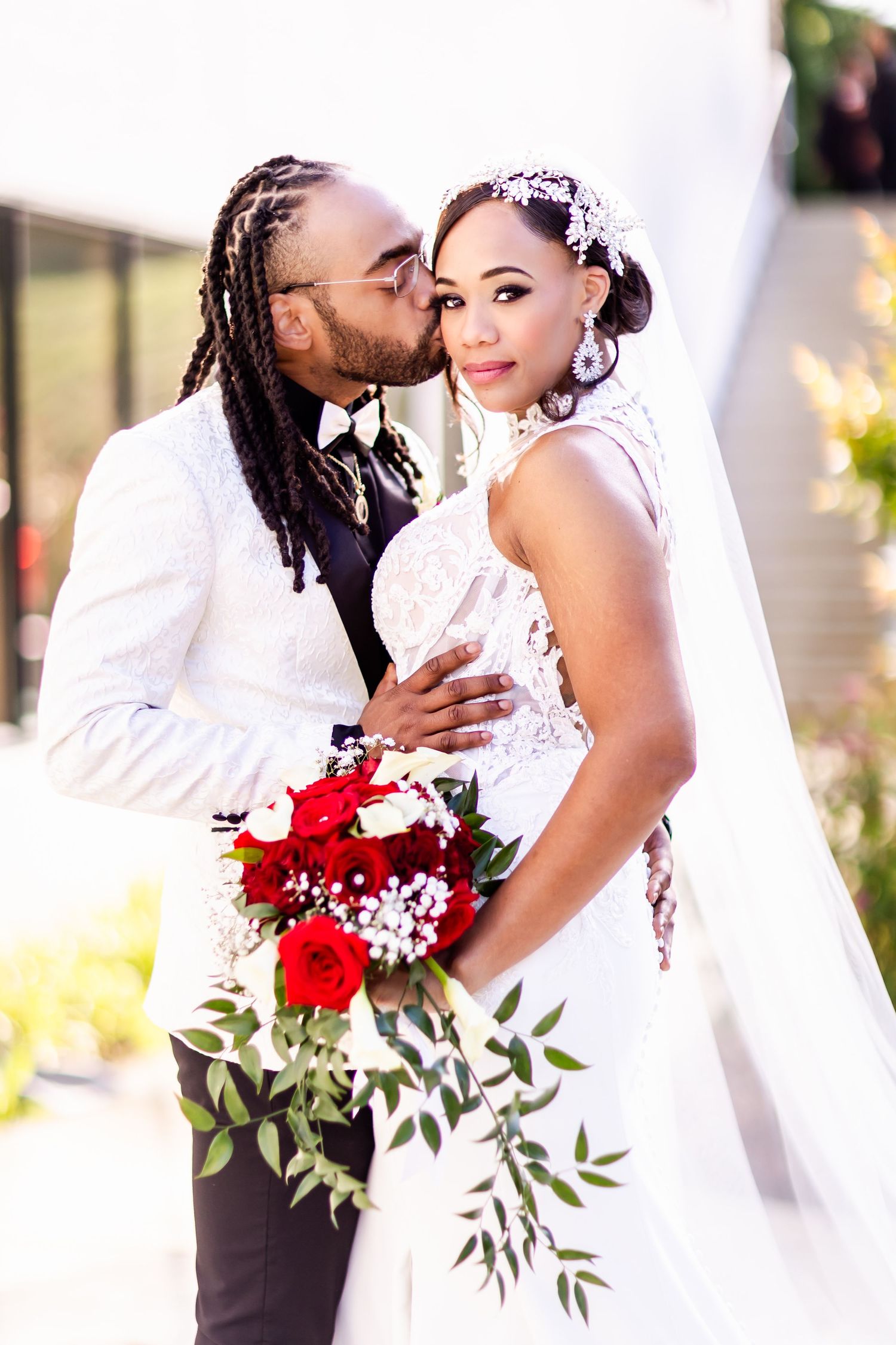 Newlywed couple sharing an intimate moment with red roses in the wedding bouquet.