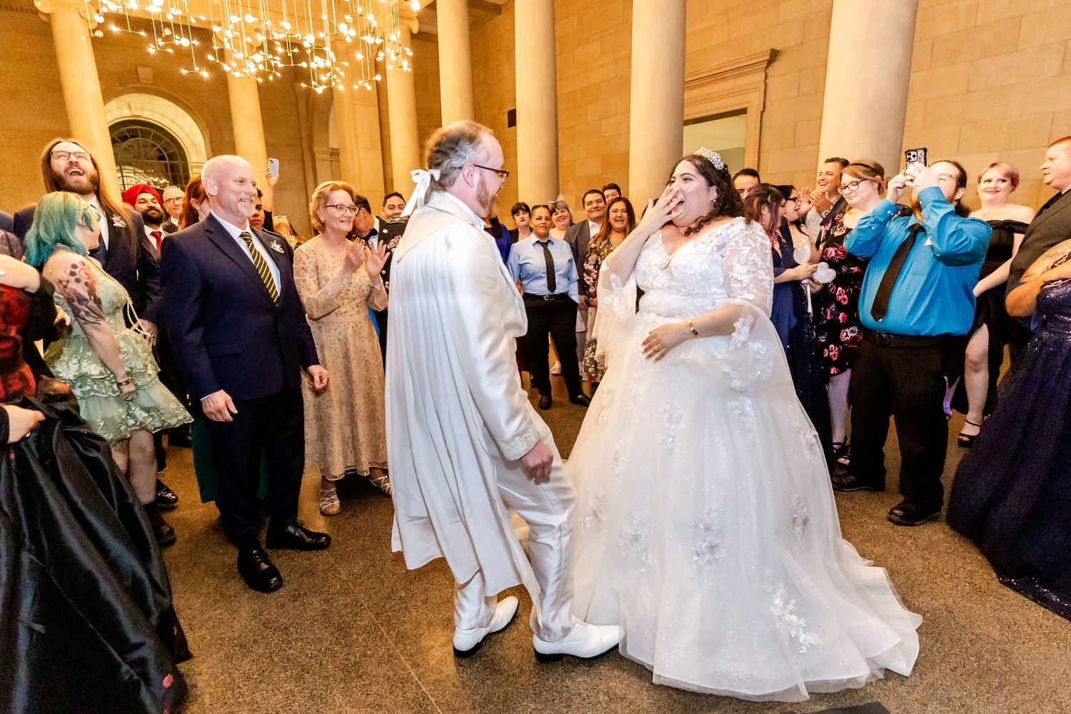 Wedding guests surround the dancing couple in an elegant venue with classical architecture.