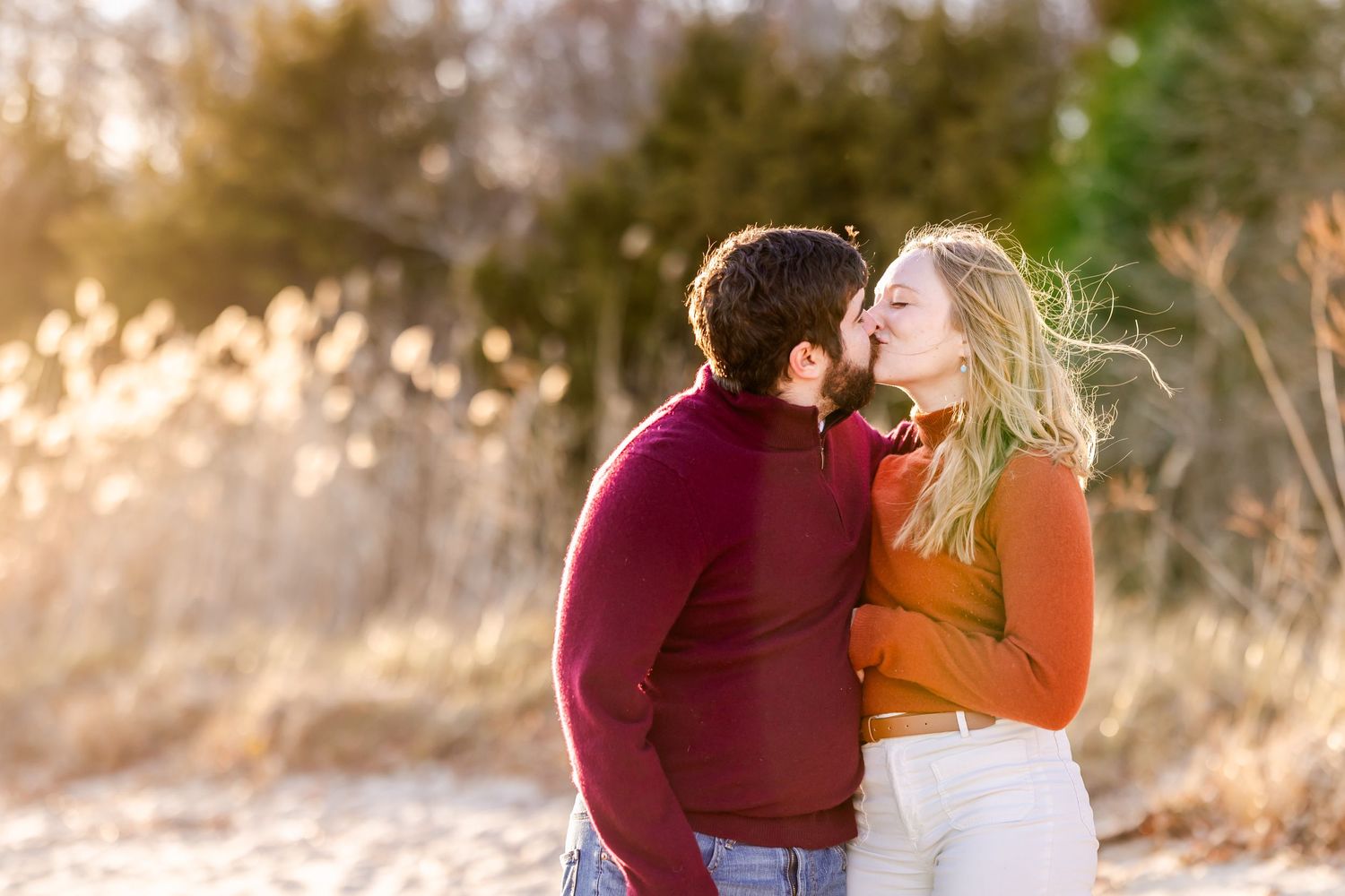 Couple in burgundy and orange sweaters share romantic moment during sunset.