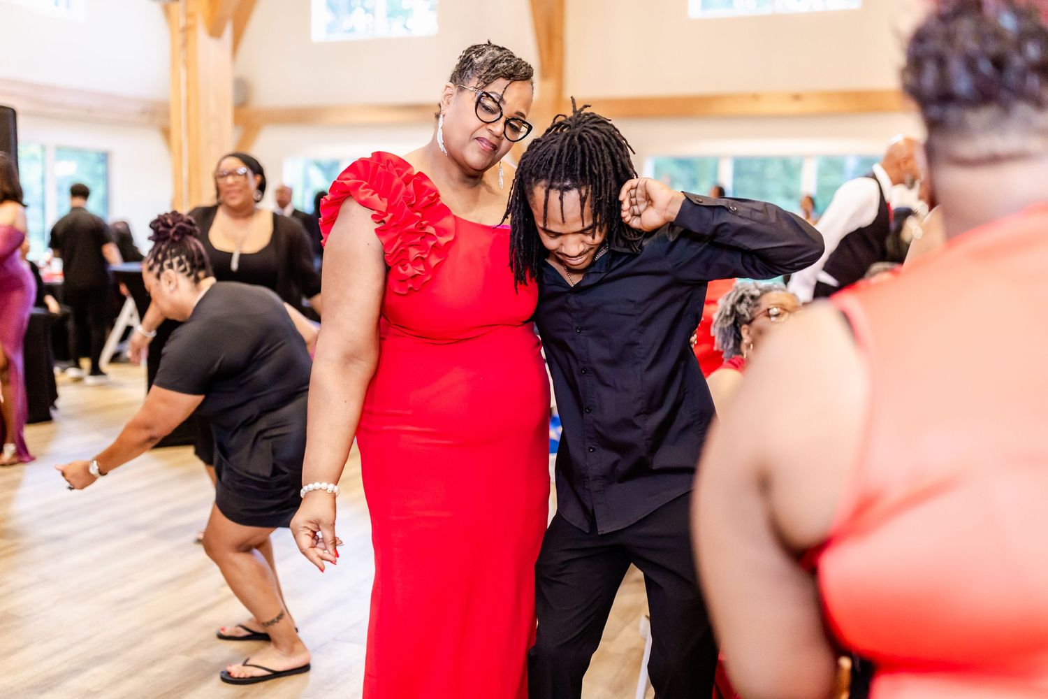 Party guests dancing together at a celebration with wooden beams visible overhead.