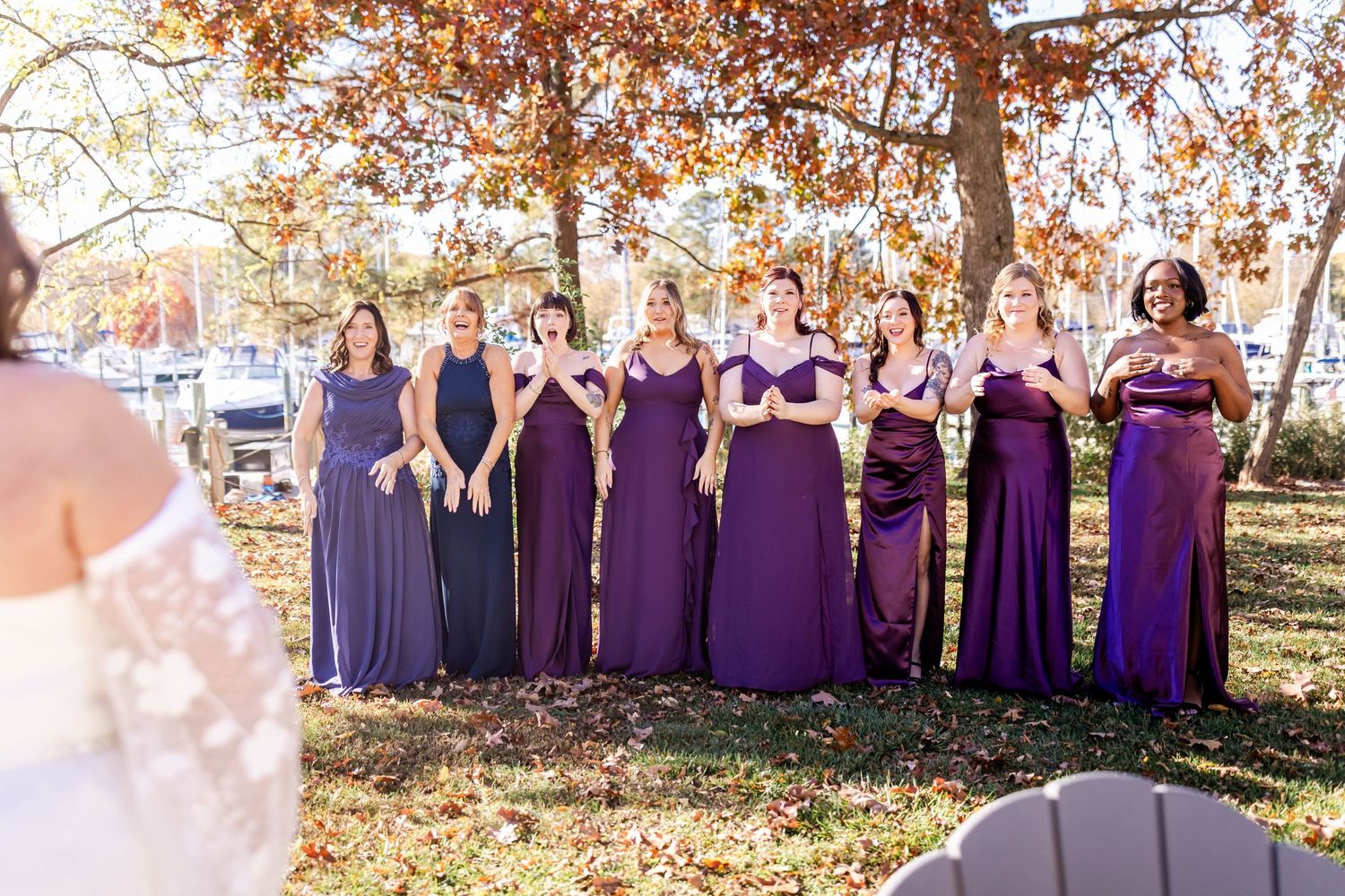 Bridesmaids in purple dresses stand in line outdoors during fall wedding.