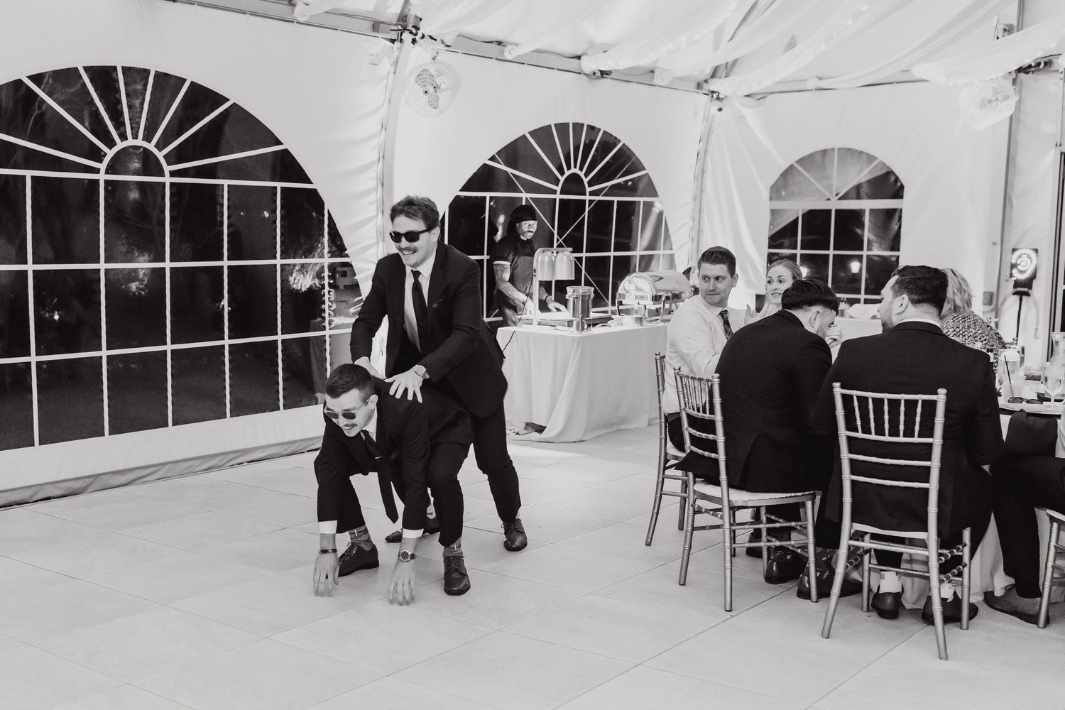 Black and white photo of guests dancing and mingling at an elegant tented reception.
