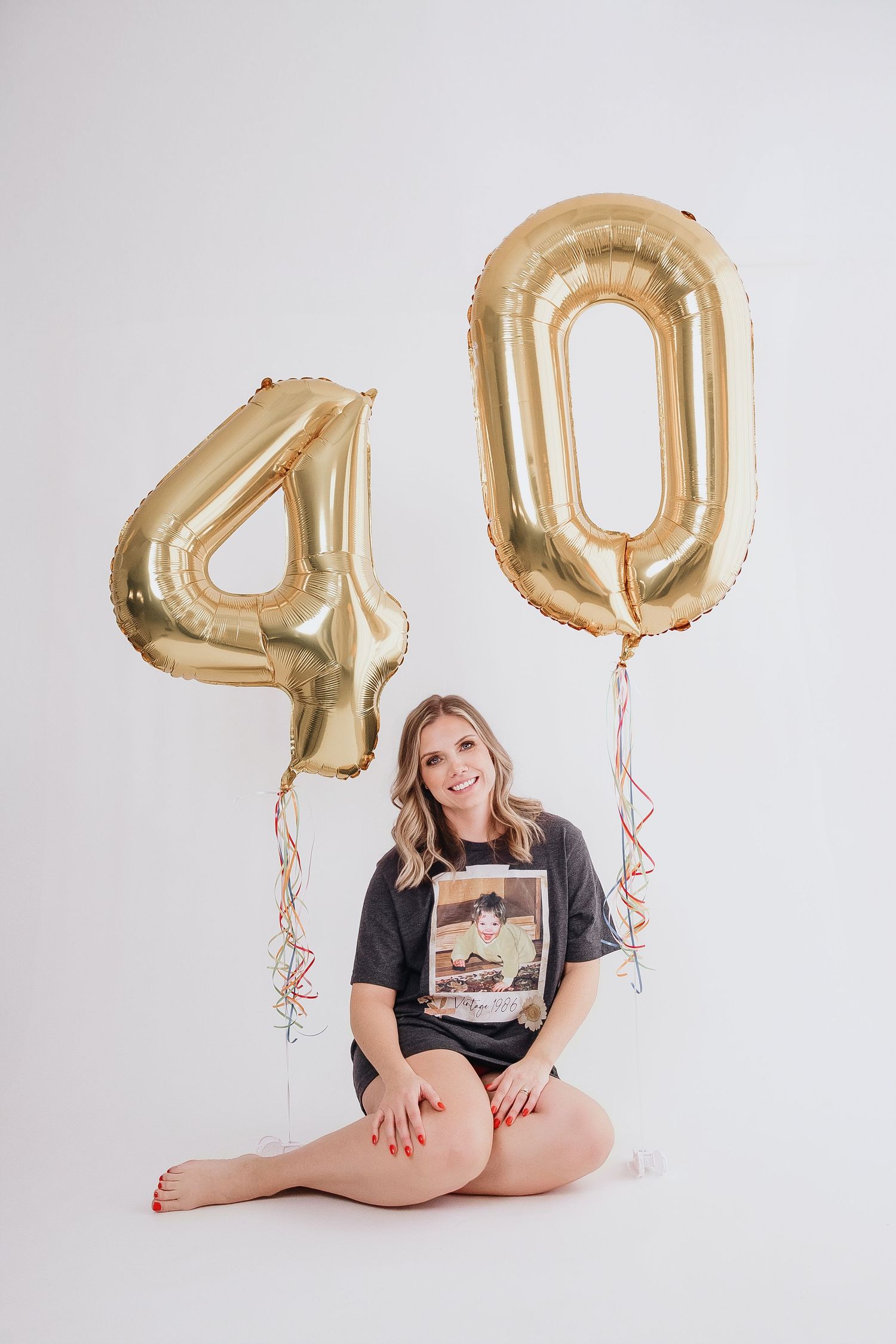 Playful poses with large gold number balloons against white backdrop.