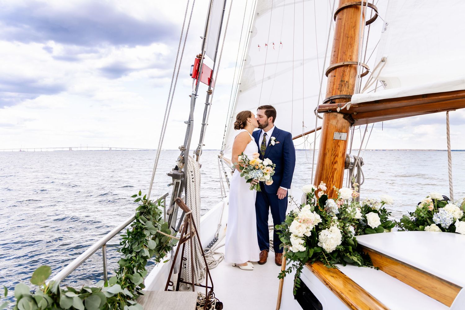A romantic sailing ceremony aboard a classic wooden yacht decorated with white floral arrangements and greenery.