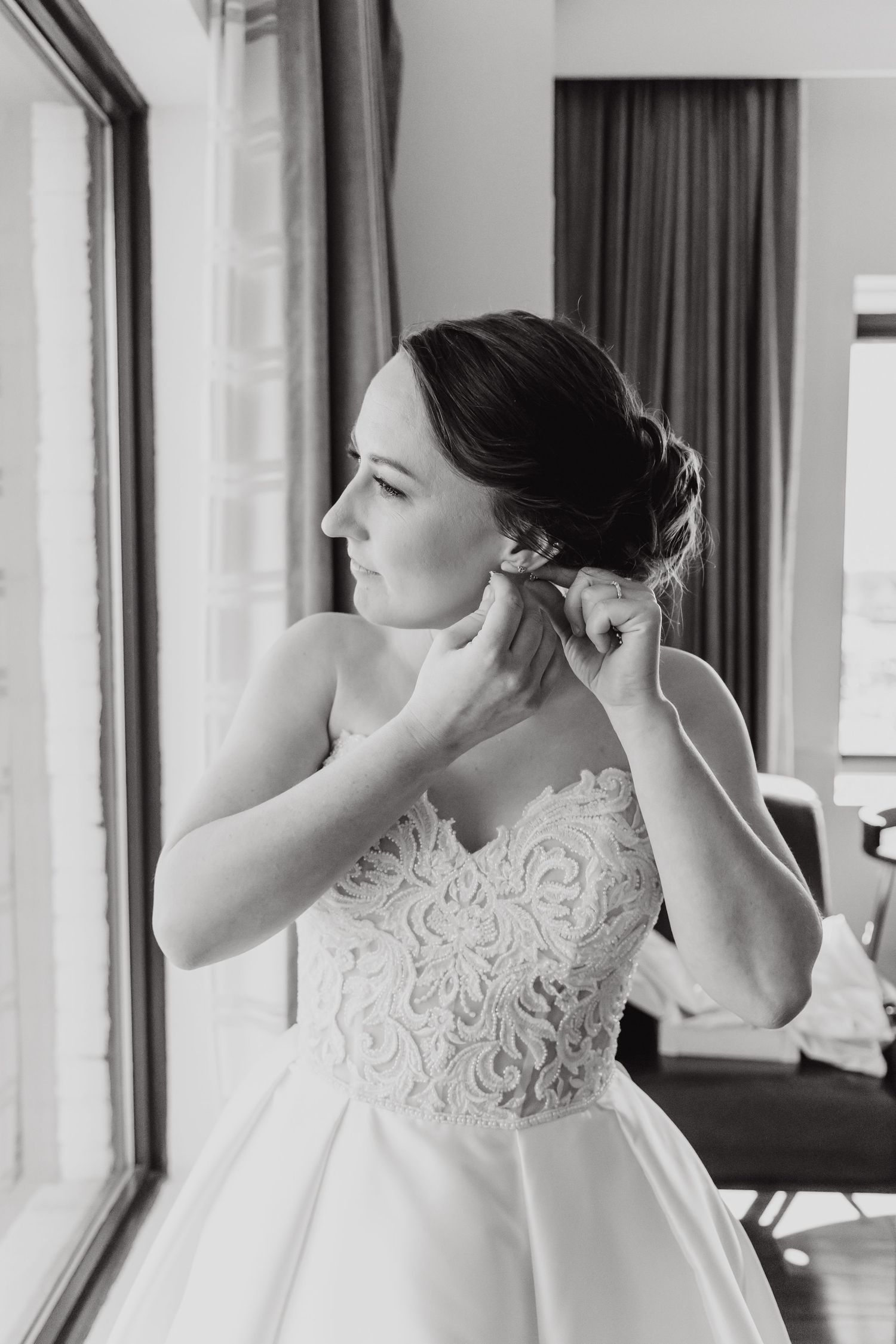 Black and white photo of a bride in a lace wedding dress laughing joyfully near a window.