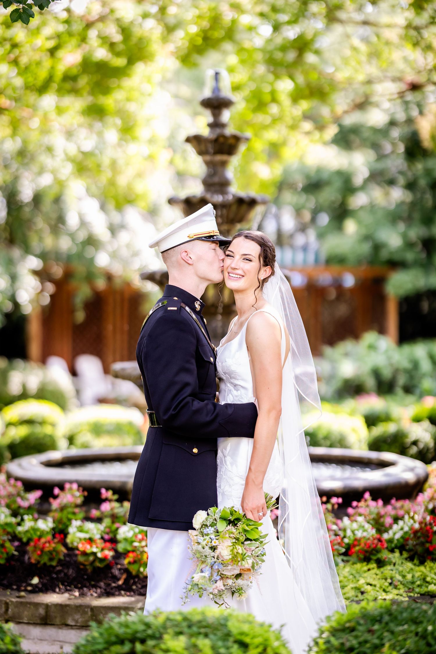 Military wedding couple shares romantic moment in garden with fountain and flowers.